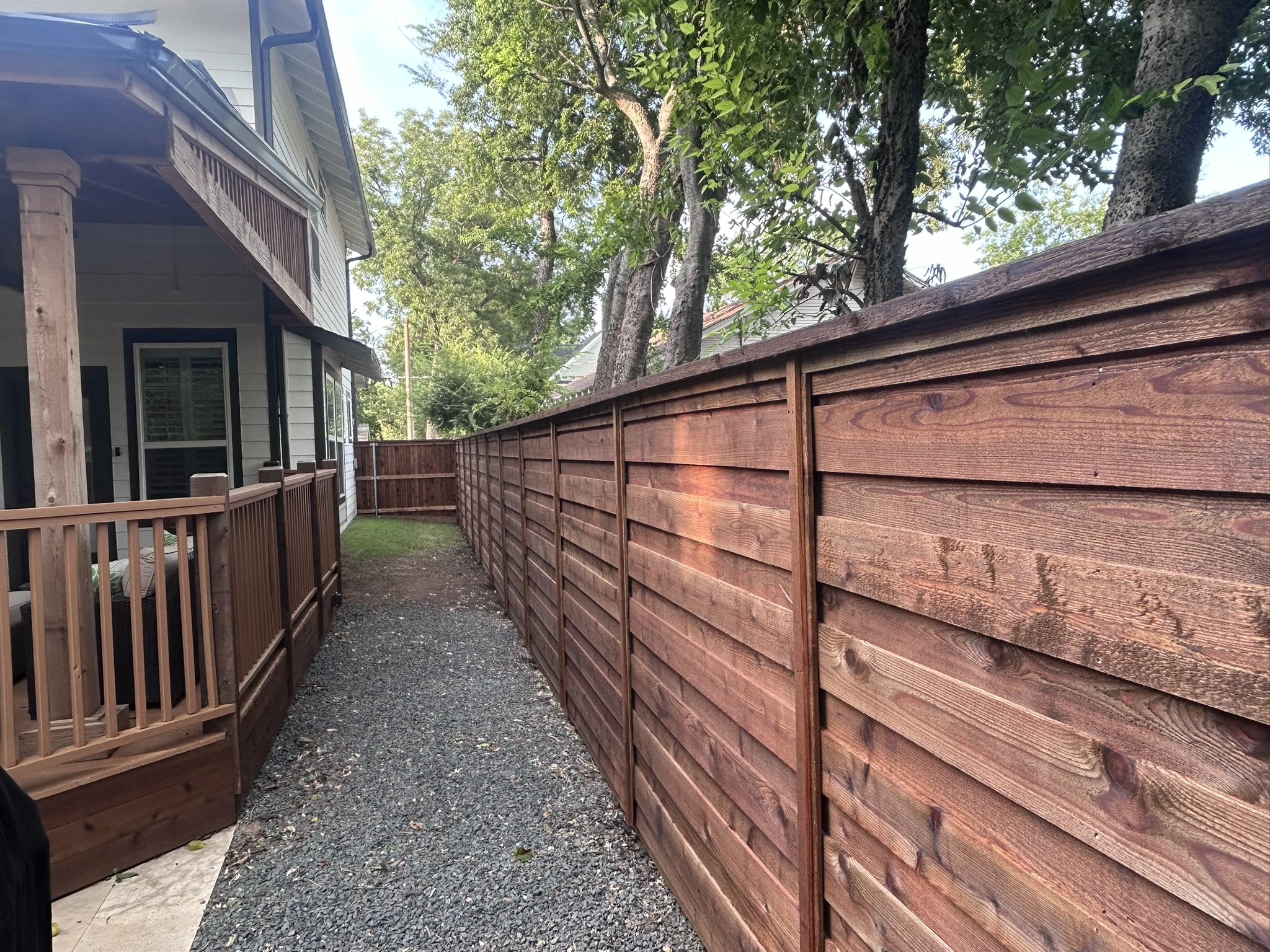 Horizontal slat cedar fence along a gravel pathway beside a house with deck