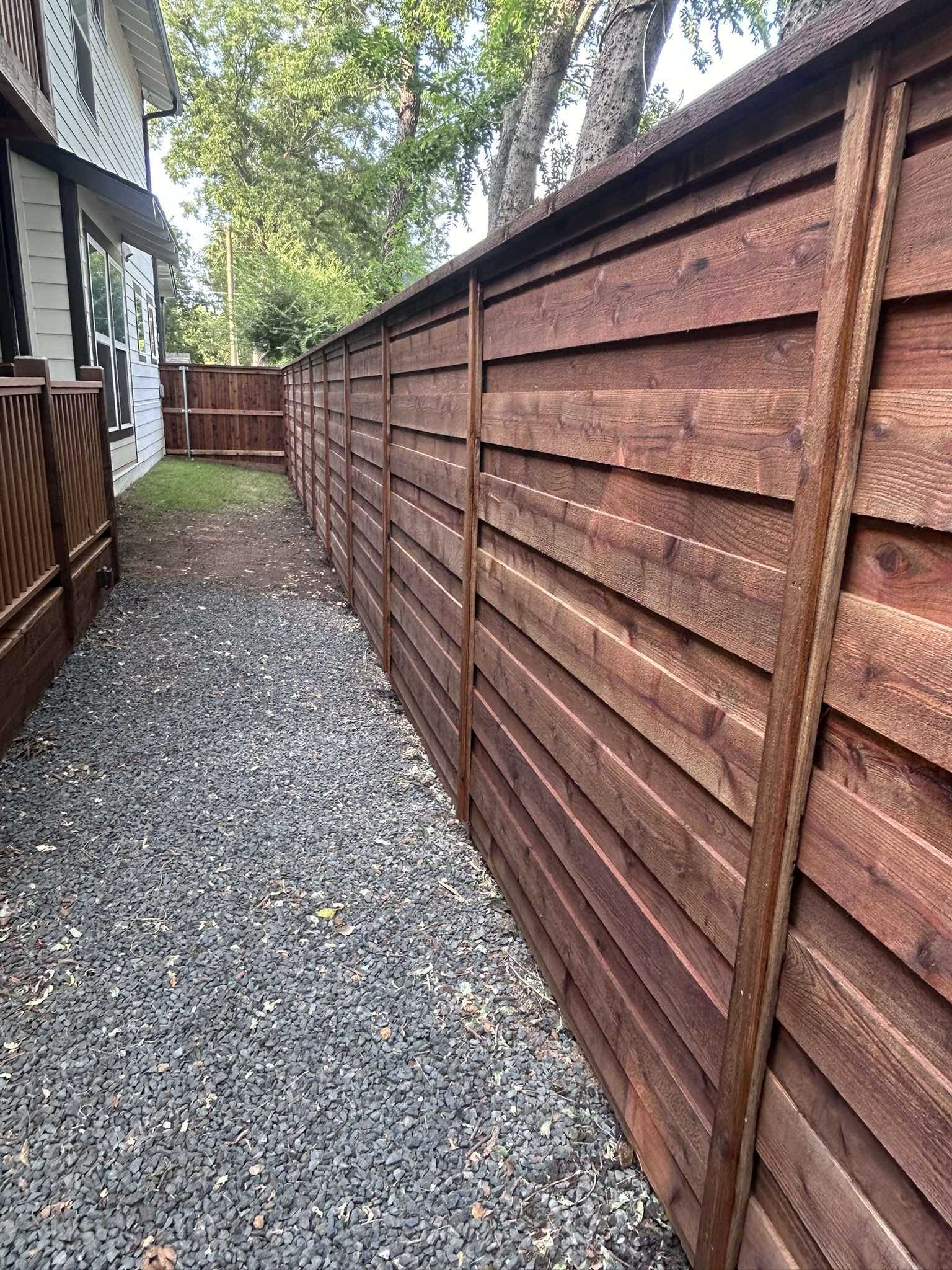 Stained horizontal slat cedar fence along a gravel side yard walkway