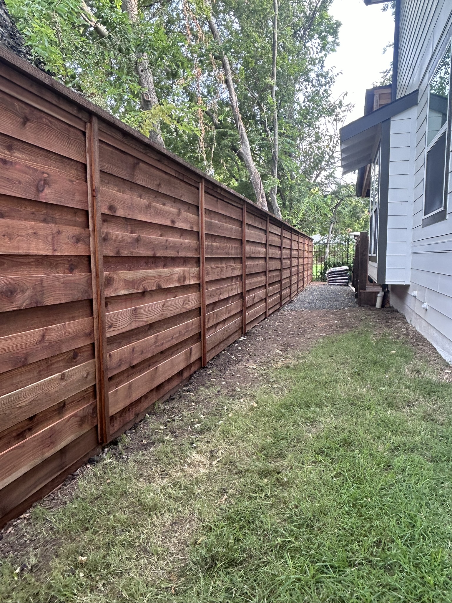 Horizontal slat cedar privacy fence running along a side yard with grass