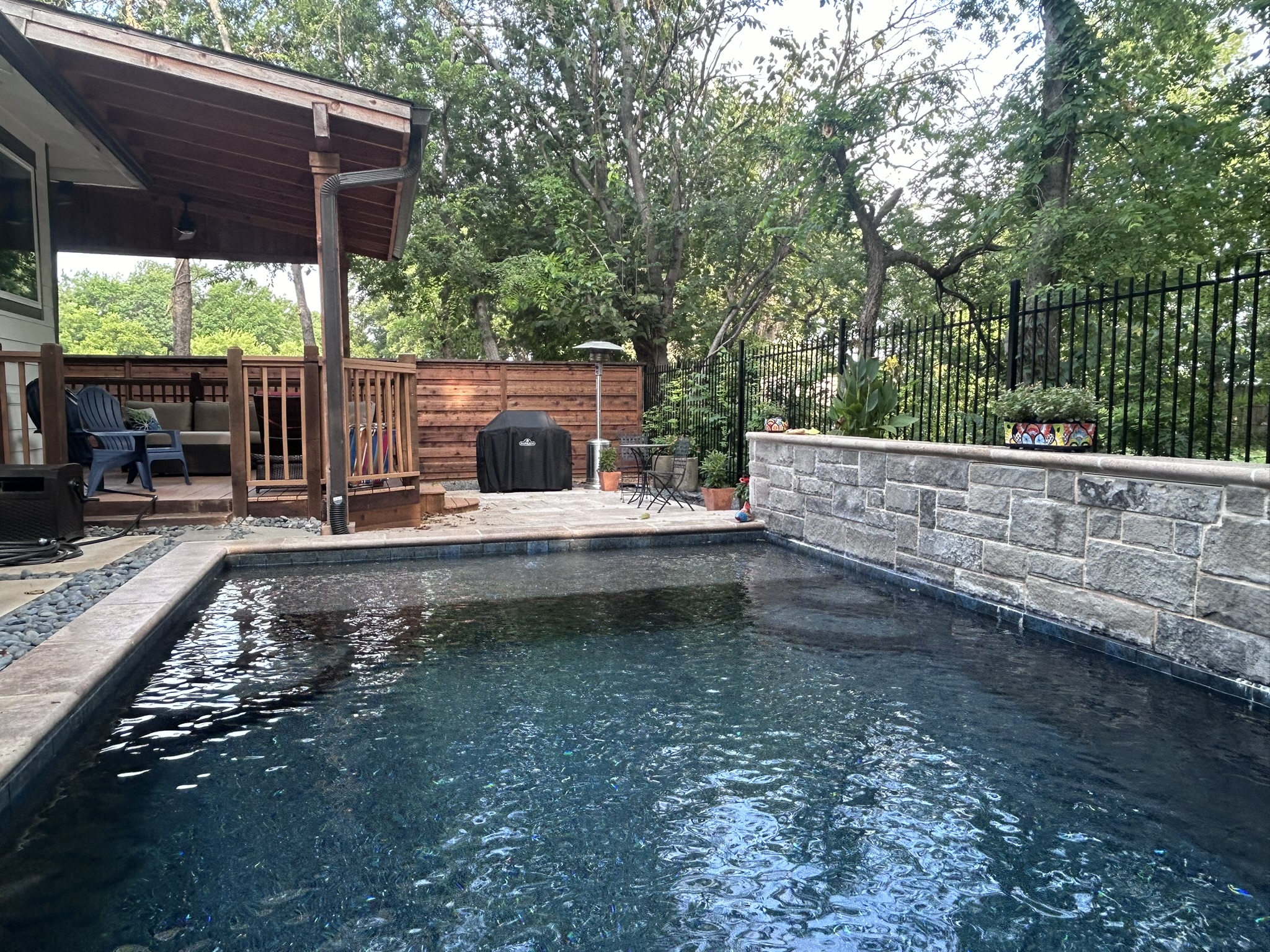 Pool area with horizontal cedar fence panel patio cover and black iron fencing