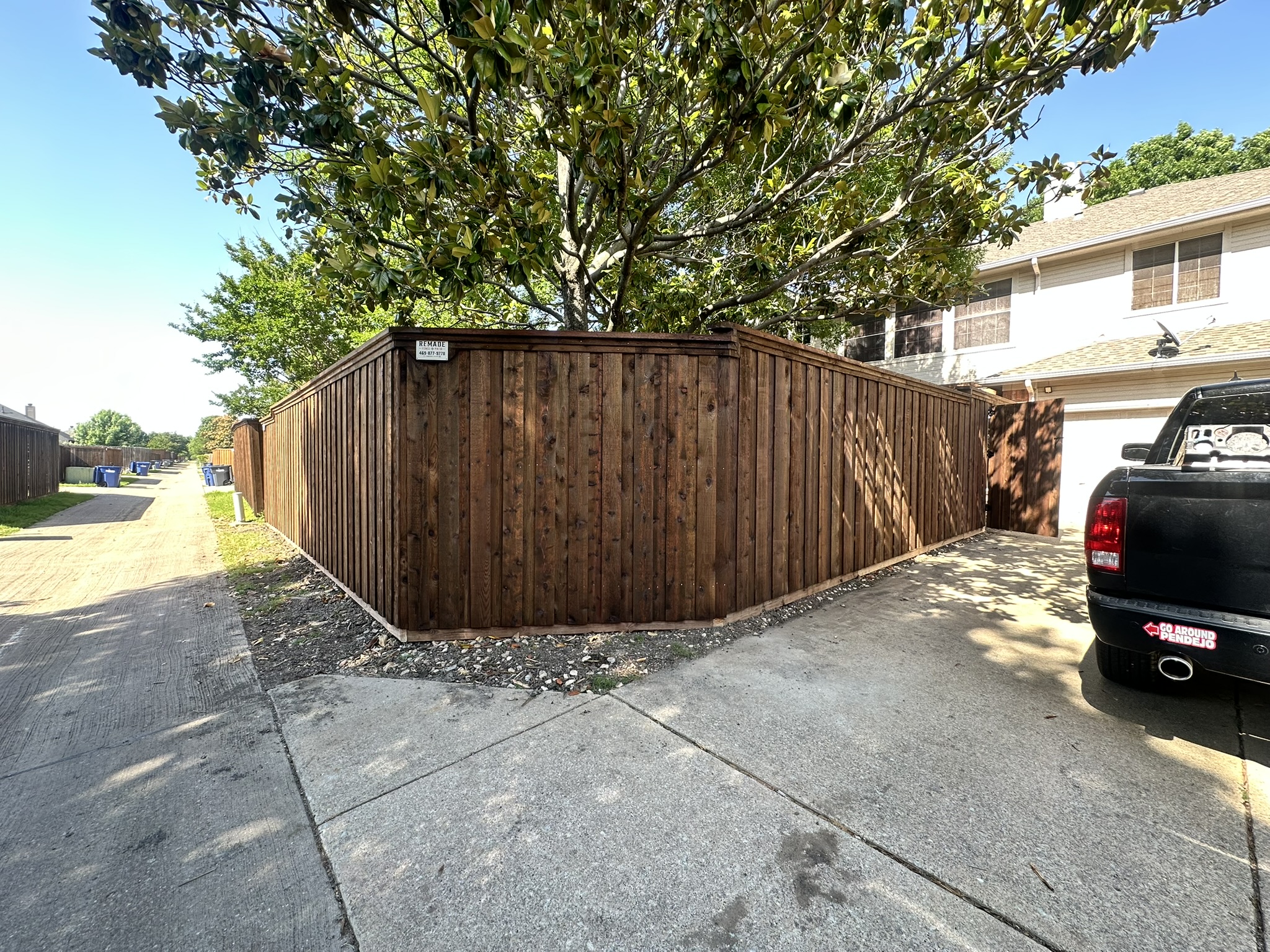 Stained cedar board-on-board privacy fence along a driveway with large tree