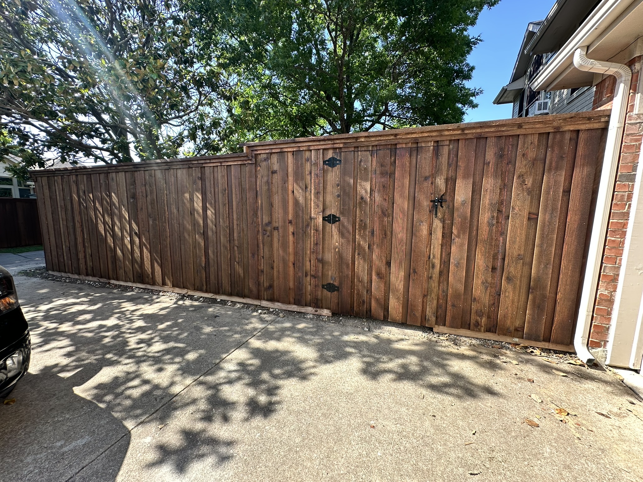 Stained cedar privacy fence with gate along a driveway beside a brick house