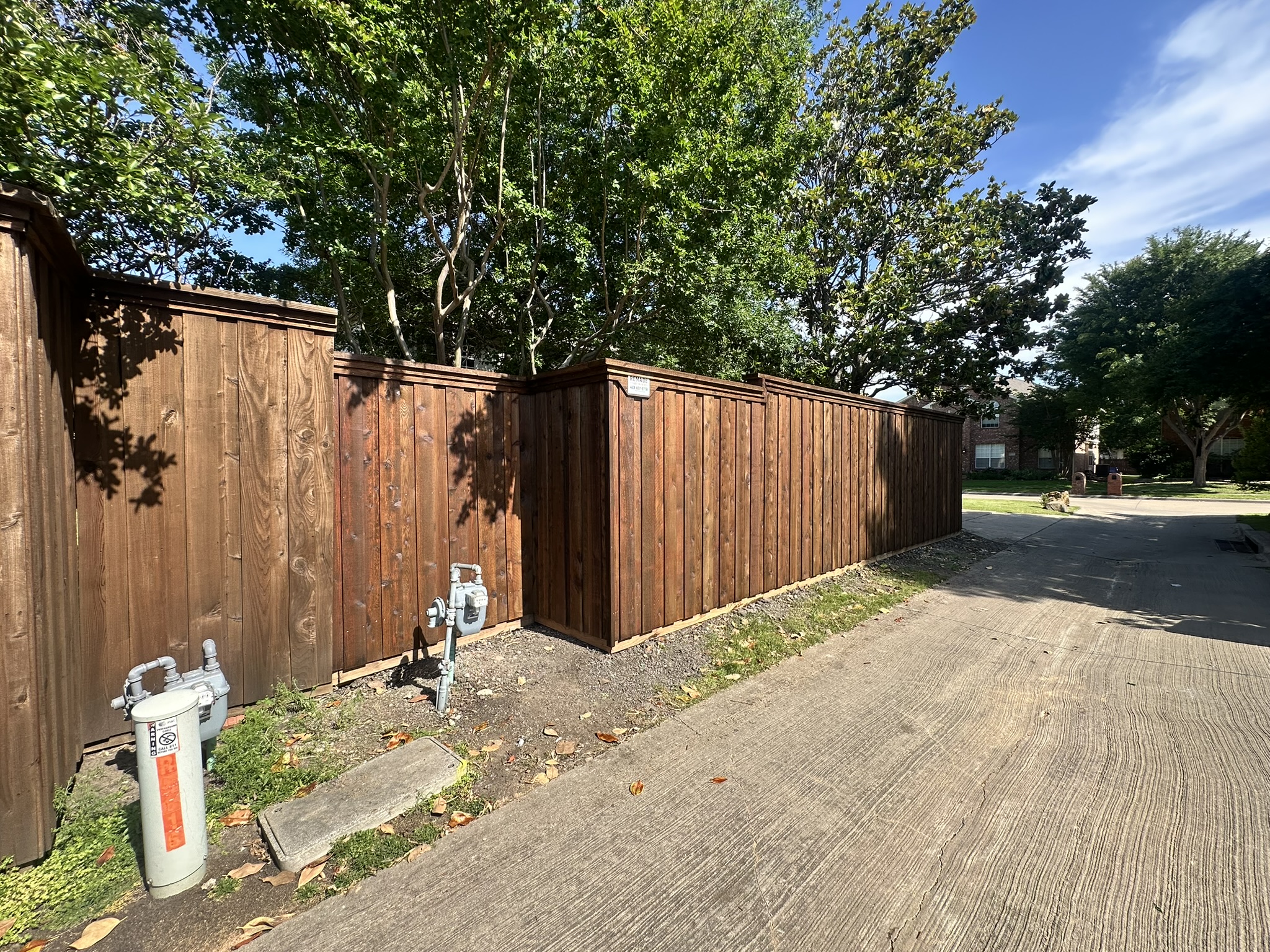 Stained cedar board-on-board fence viewed from driveway side with utility meters