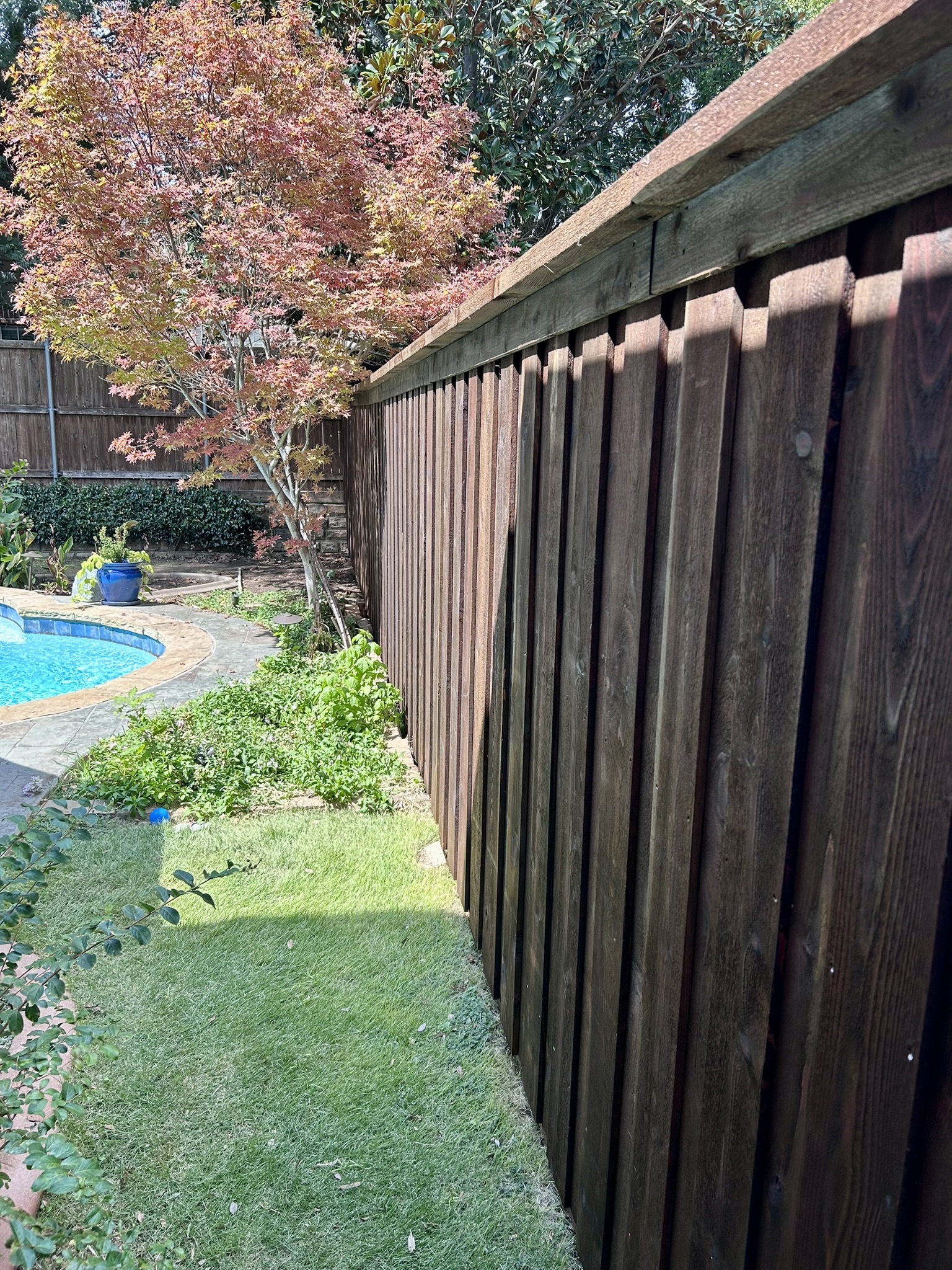 Stained cedar fence section next to a brick house with gutter downspout