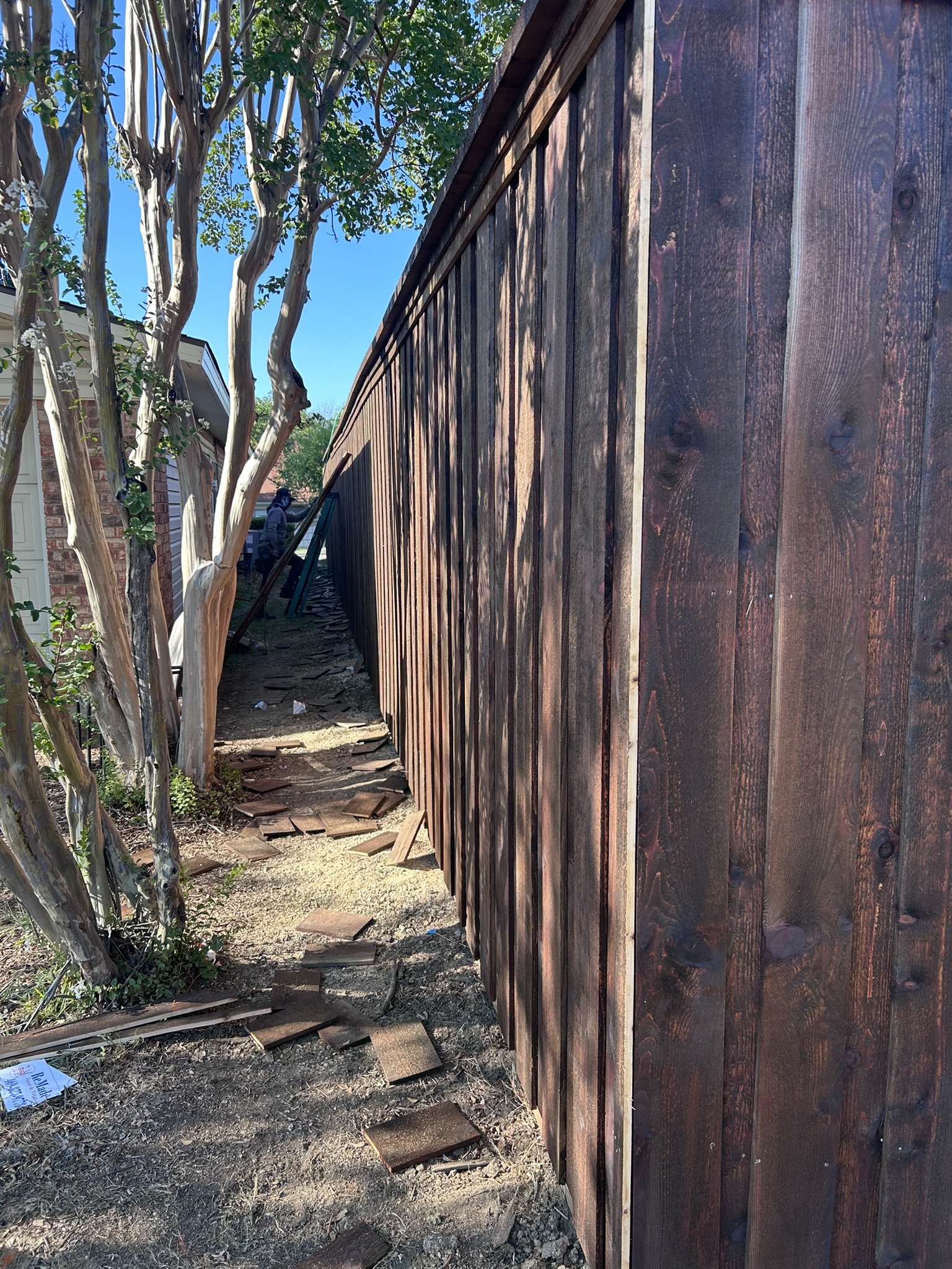 Tall dark stained cedar board-on-board privacy fence along a dirt yard