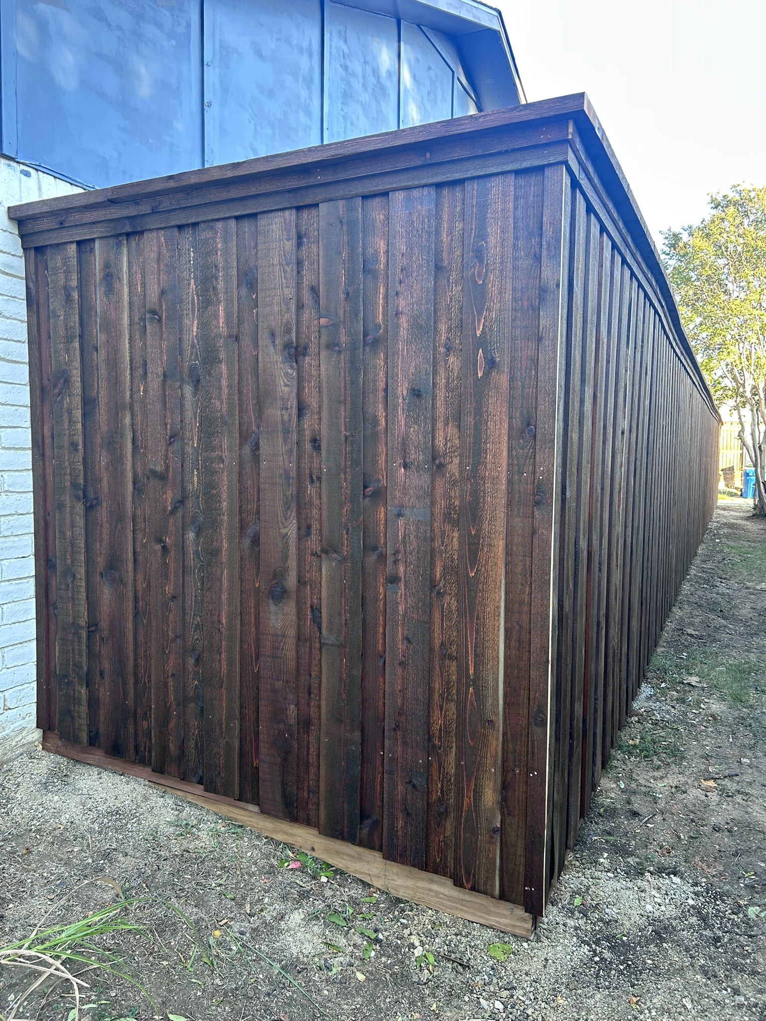 Dark-stained cedar board-on-board privacy fence corner next to a house