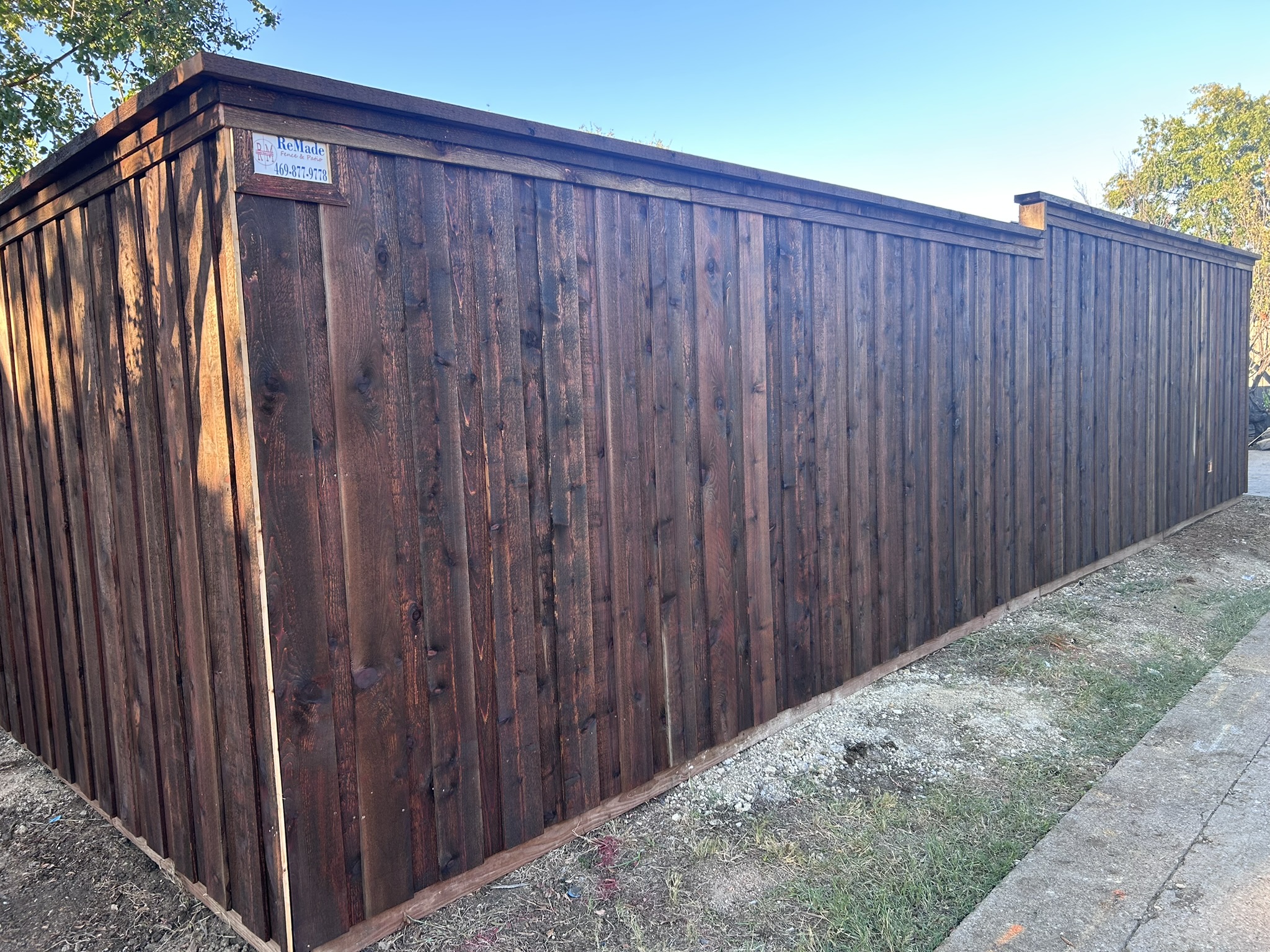 Long dark-stained cedar board-on-board privacy fence with cap rail and trim