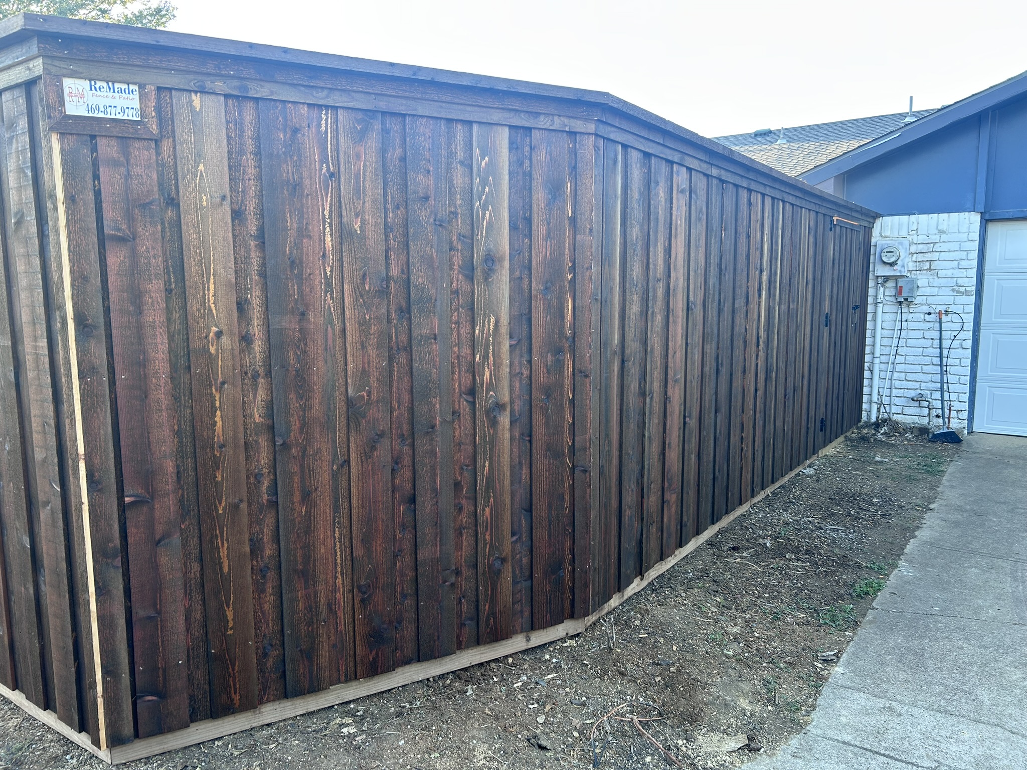 Dark-stained cedar privacy fence with cap rail next to a driveway and garage