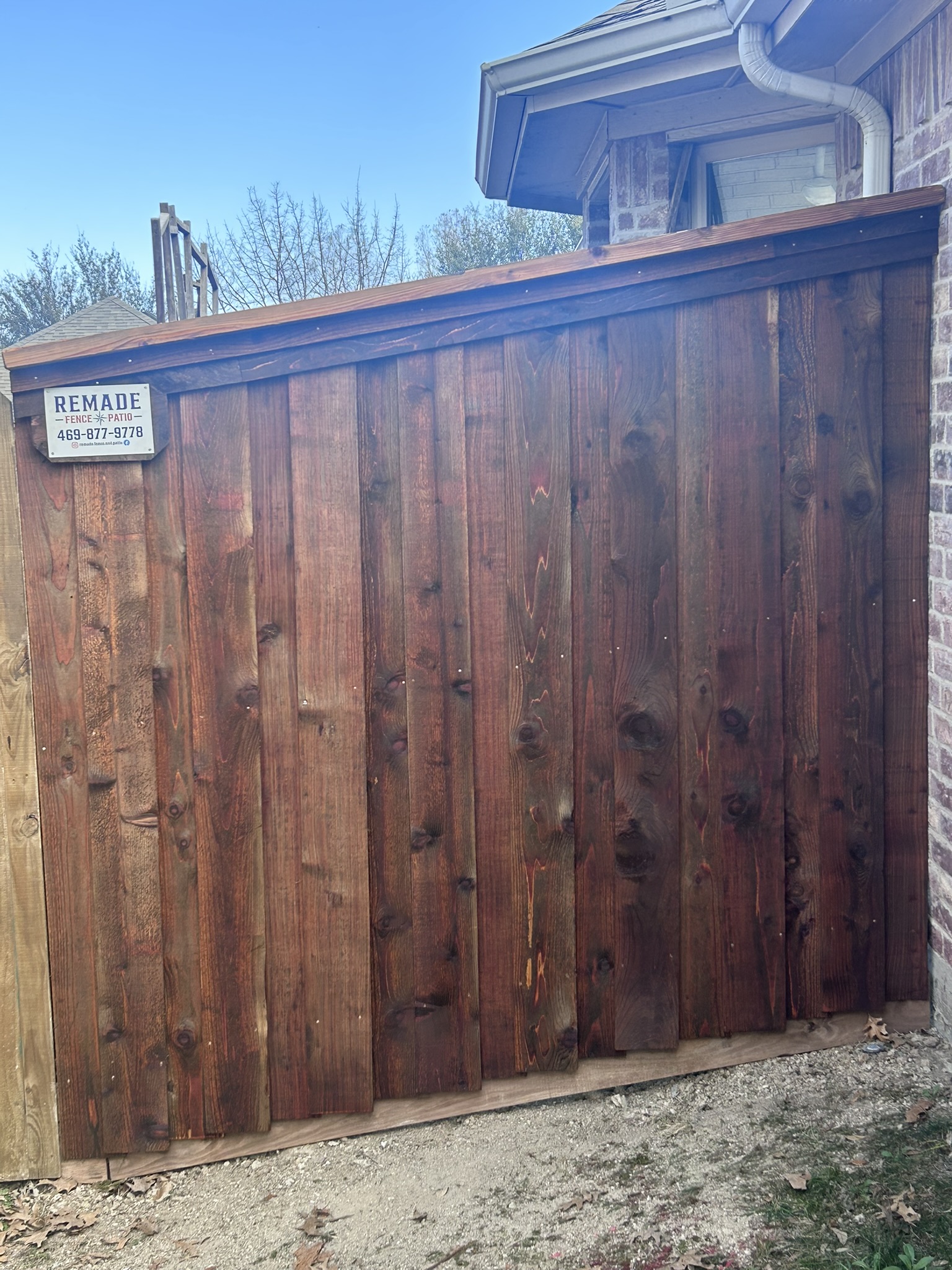Dark-stained cedar privacy fence section with cap rail next to a brick house