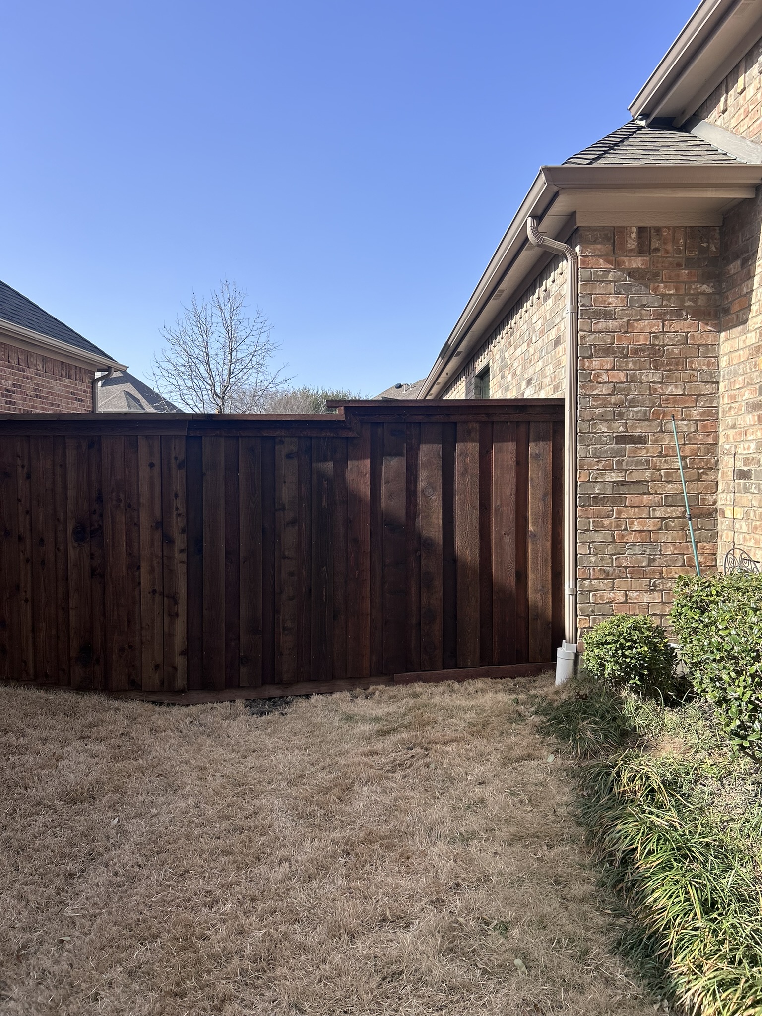 Dark-stained cedar privacy fence beside a brick home with dormant winter lawn