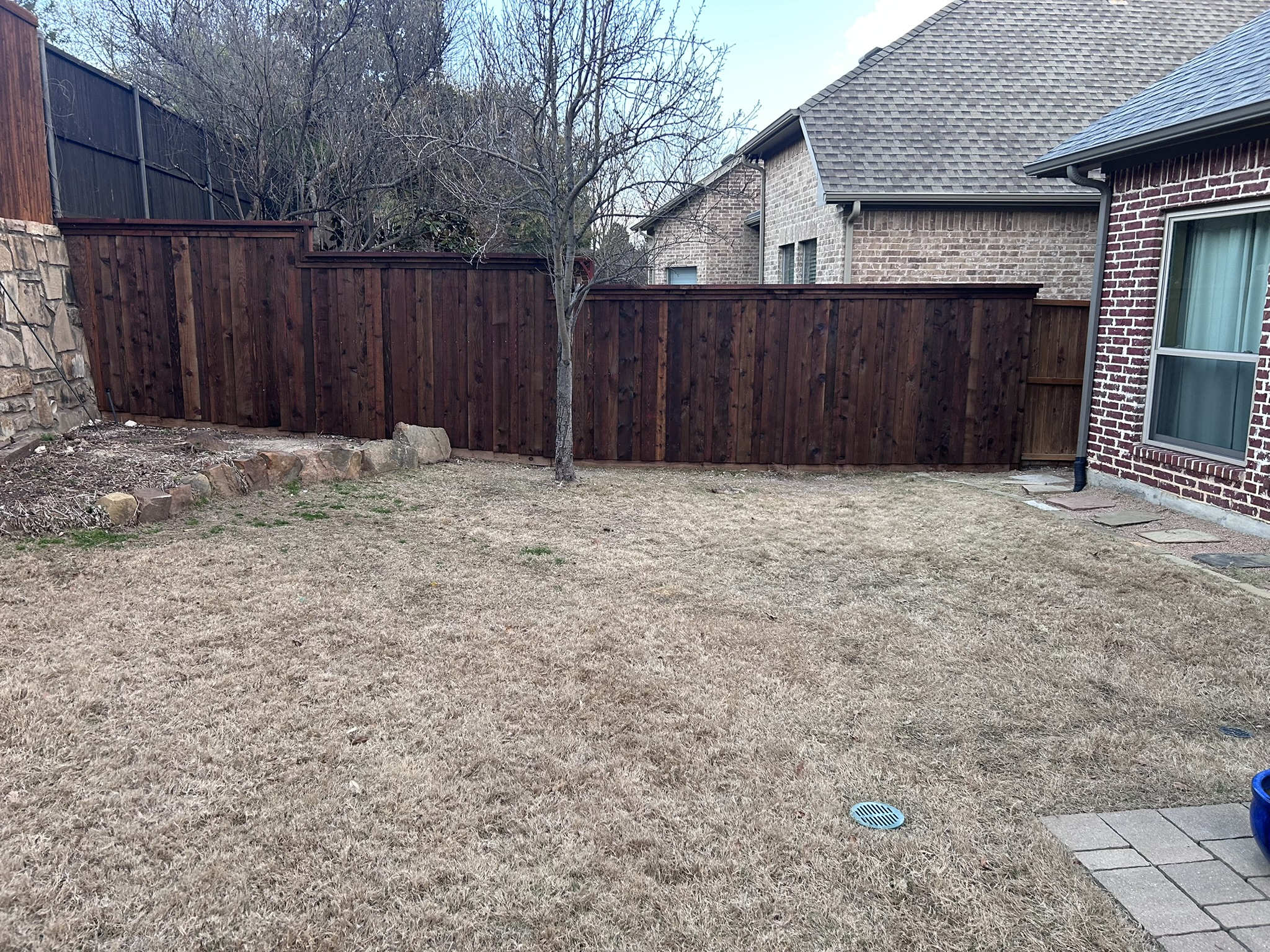 Dark-stained cedar privacy fence across a backyard with stone accents and brick homes
