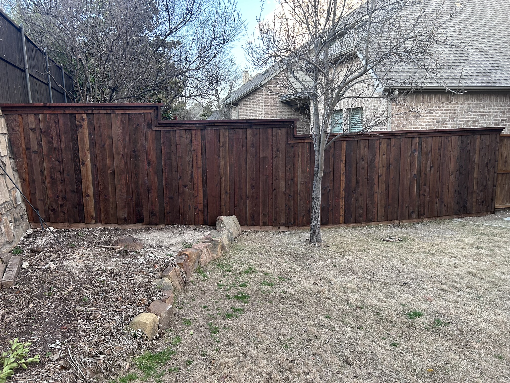 Dark-stained cedar board-on-board privacy fence in backyard with stone border