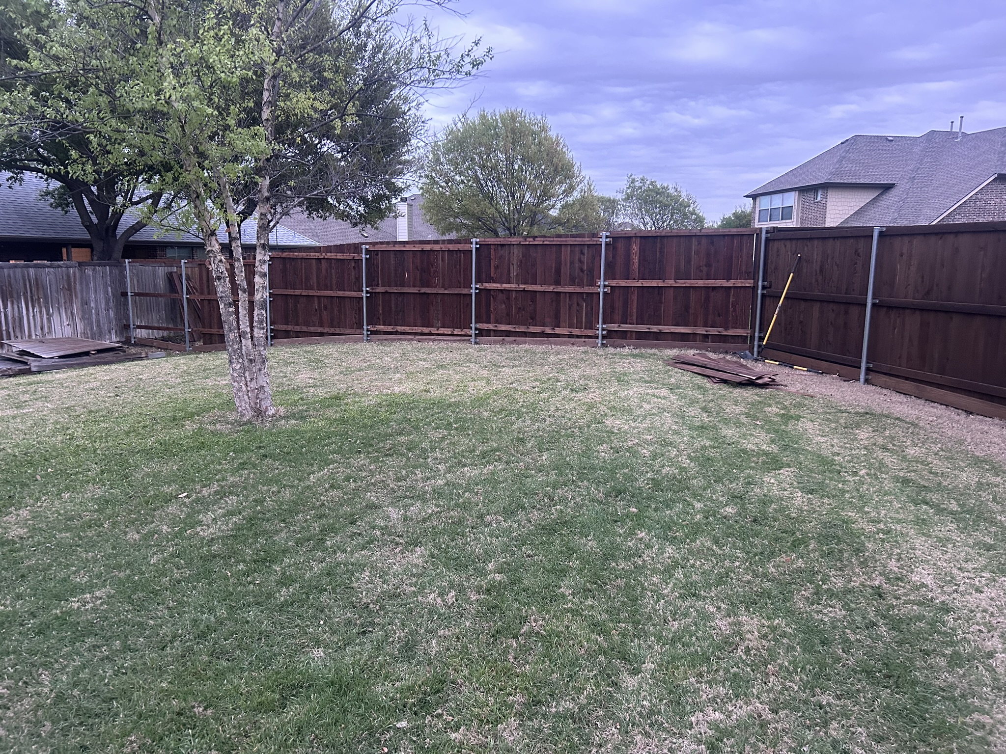 Dark-stained cedar privacy fence under construction in backyard with metal posts