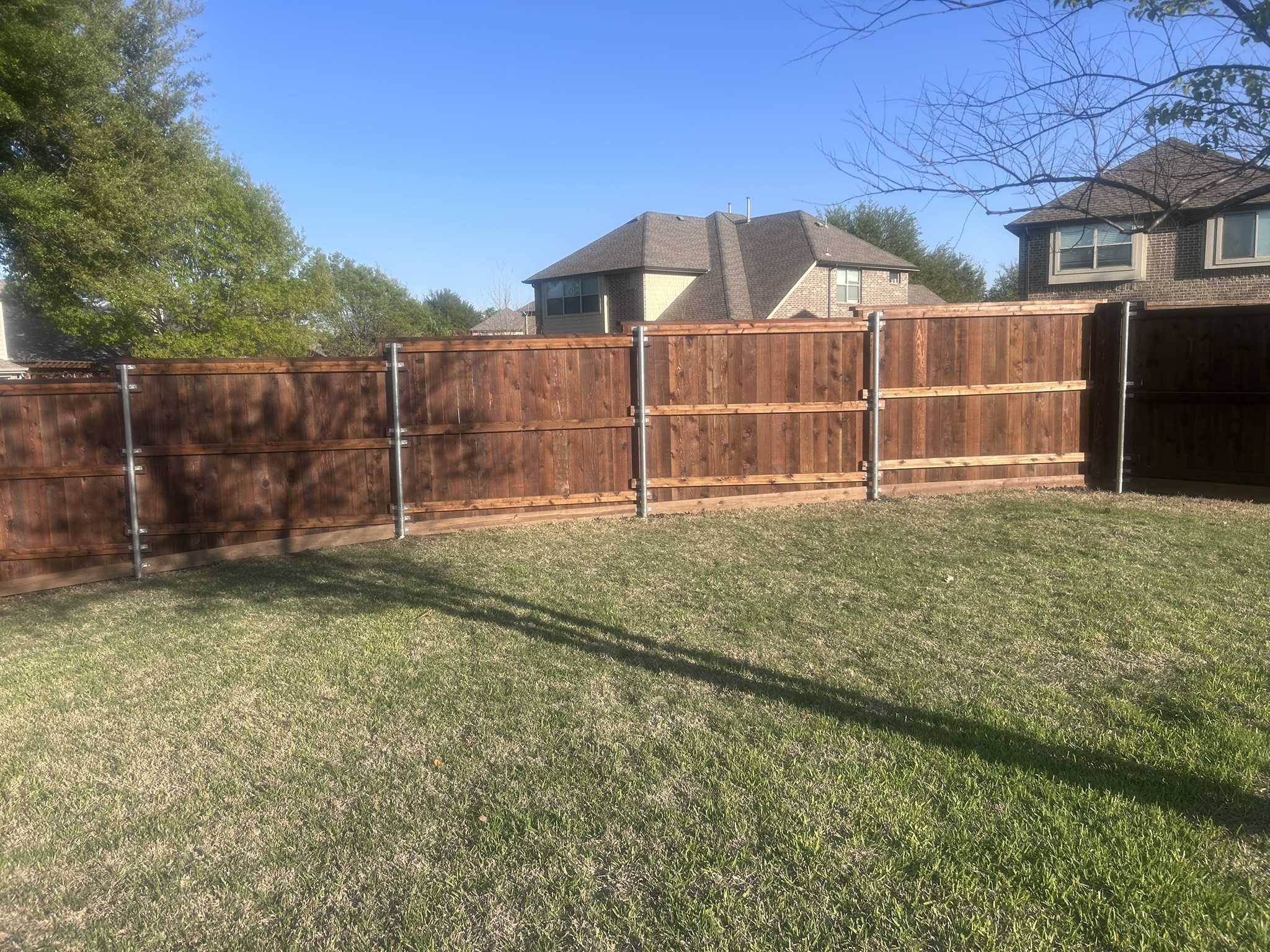 Stained cedar board-on-board fence with metal posts in a green backyard