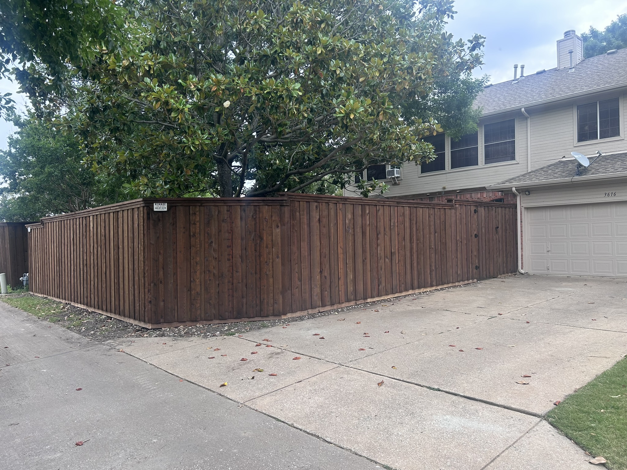 Dark-stained cedar privacy fence with trim cap running along a driveway
