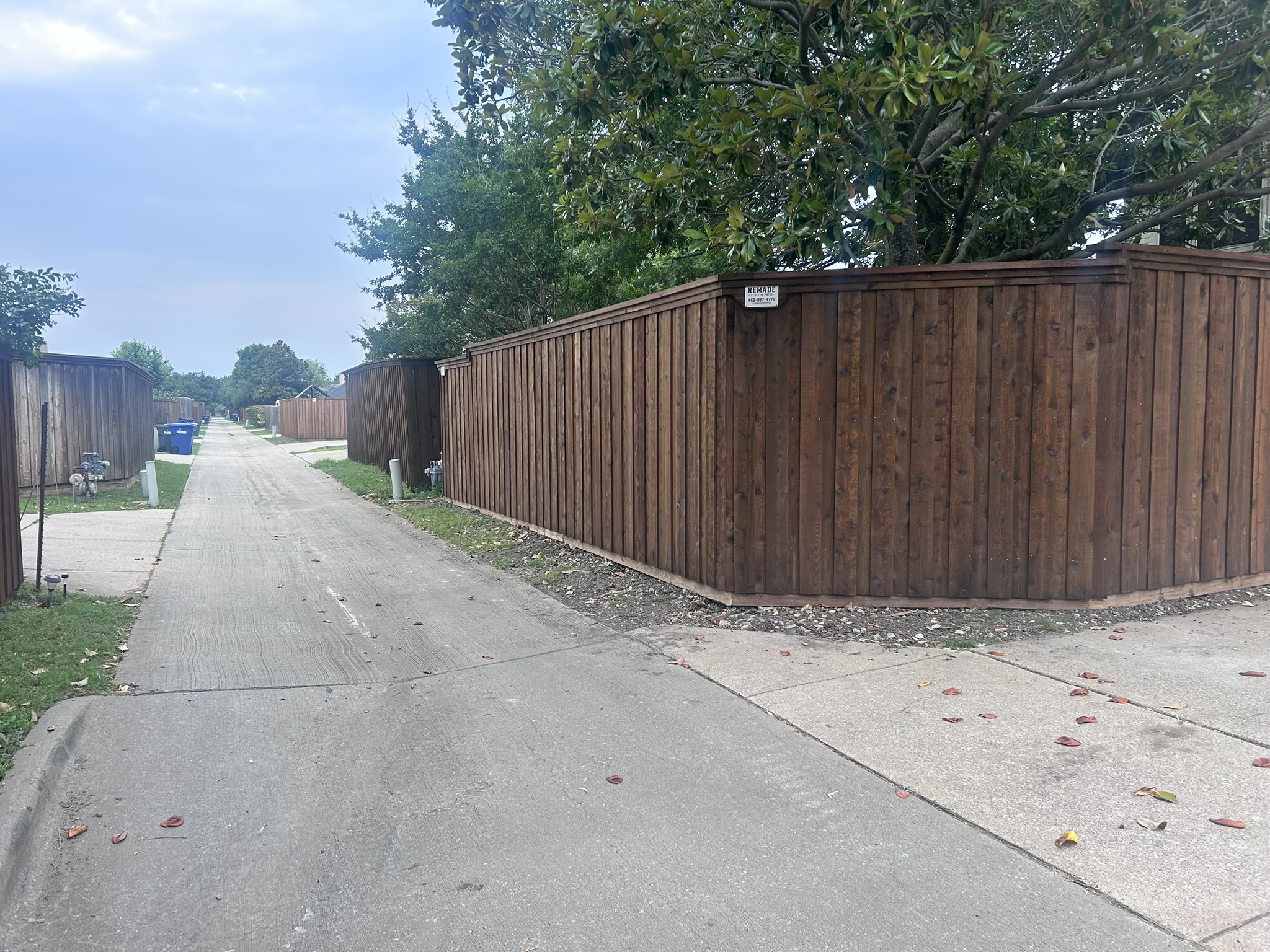 Dark-stained cedar board-on-board fence viewed from alley with company sign