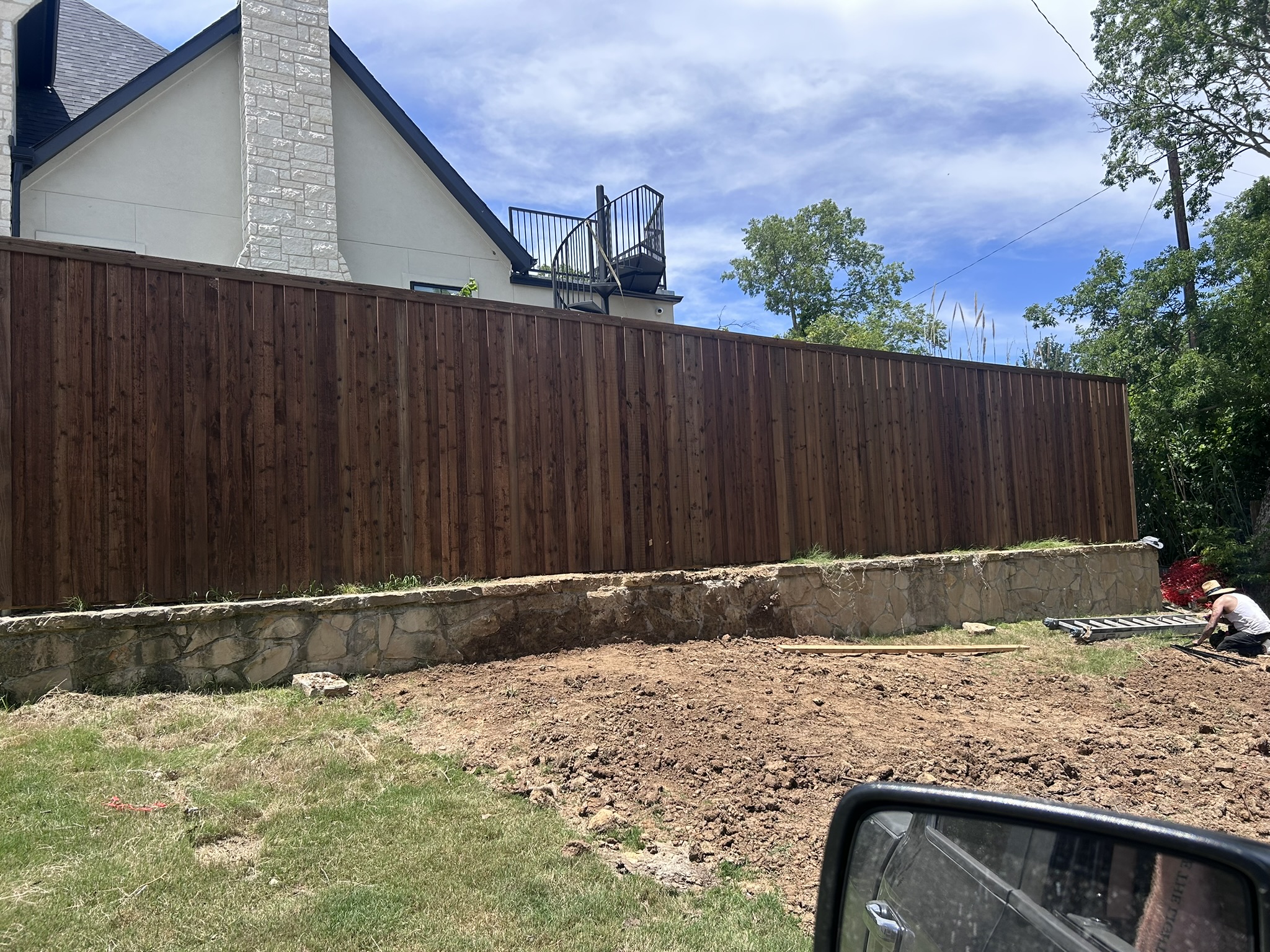Tall dark-stained cedar privacy fence on retaining wall with stone base