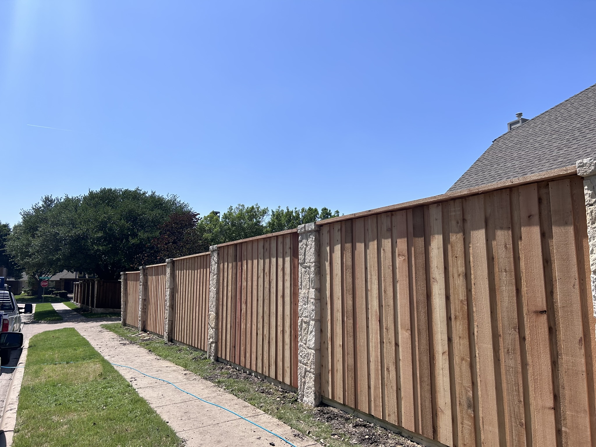 New unstained cedar board-on-board fence with stone columns along a sidewalk