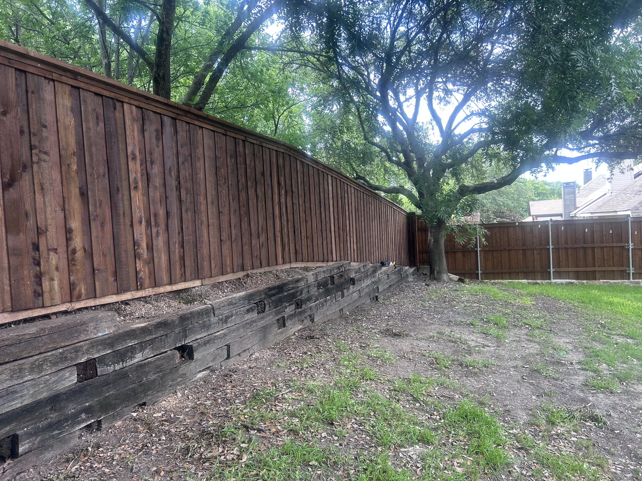 Stained cedar privacy fence with timber retaining wall base along sloped backyard