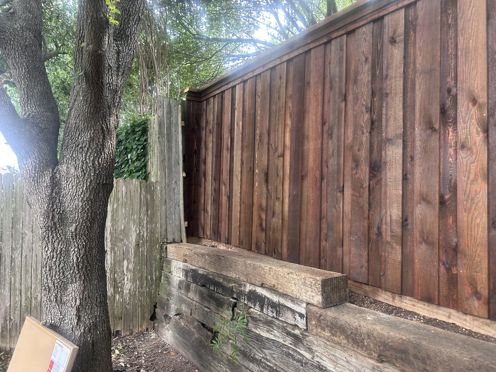 Stained cedar privacy fence above railroad tie retaining wall