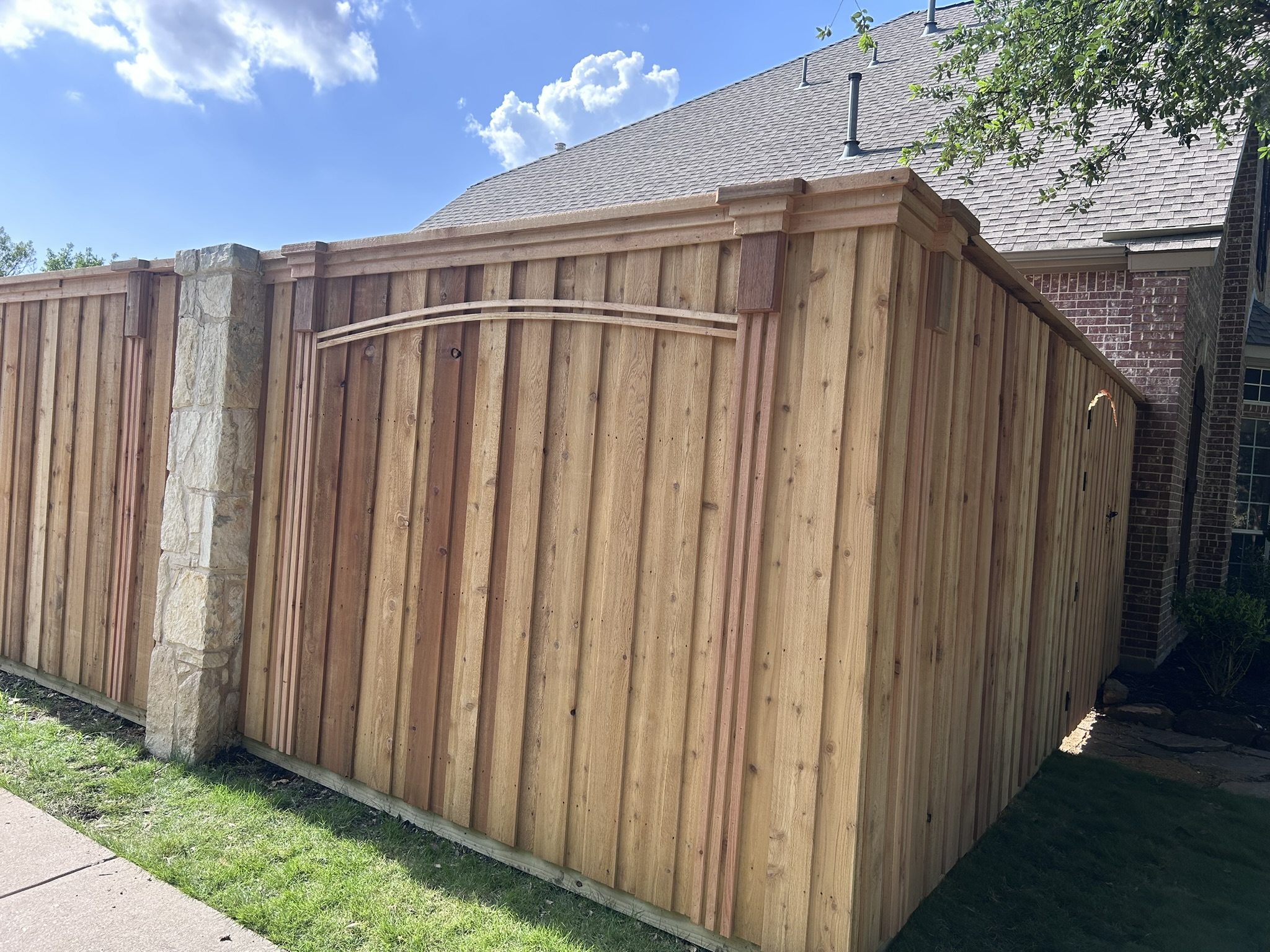 New cedar privacy fence with arched gate detail between stone columns