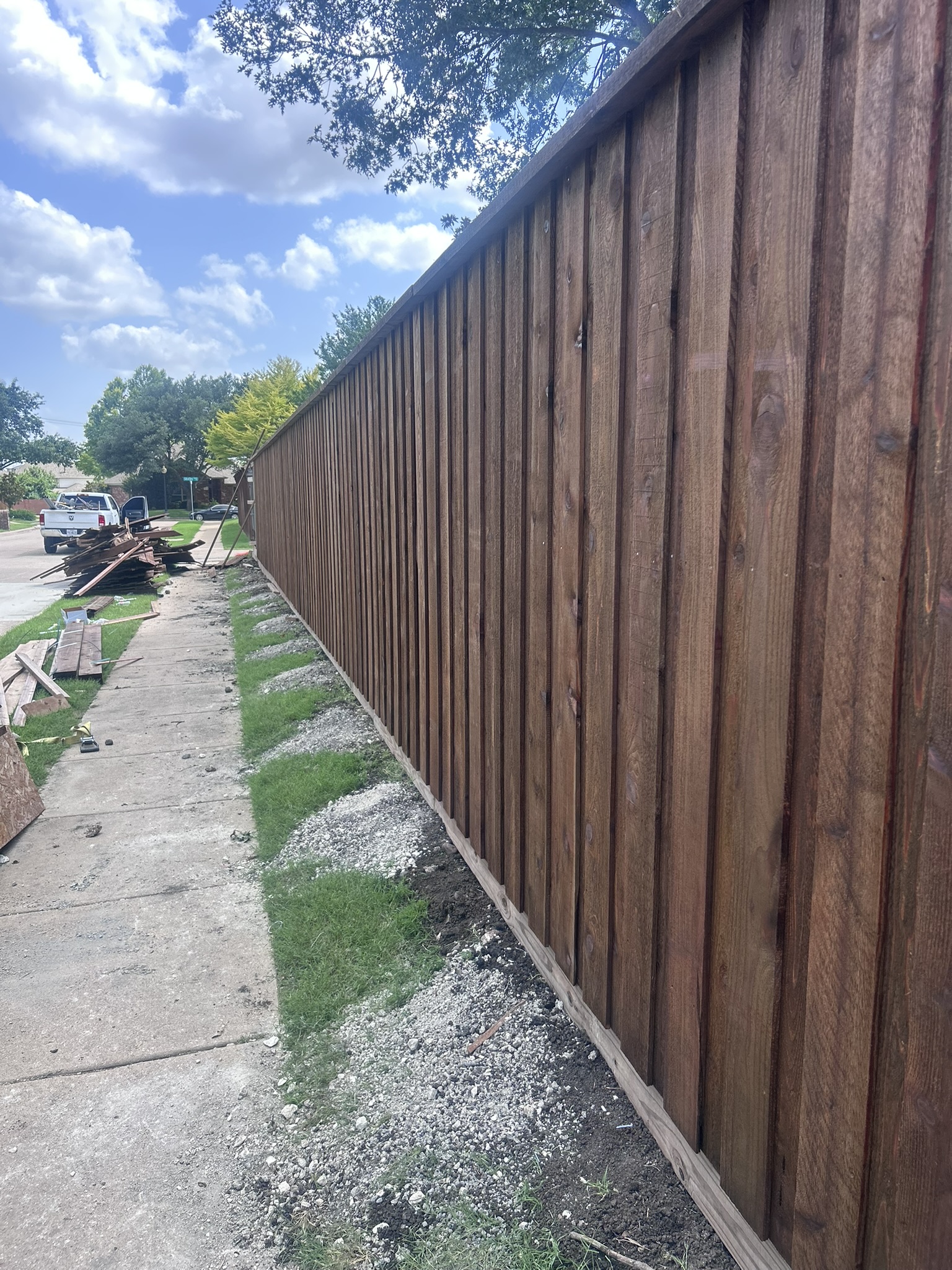 Long stained cedar board-on-board privacy fence along a sidewalk with gravel base