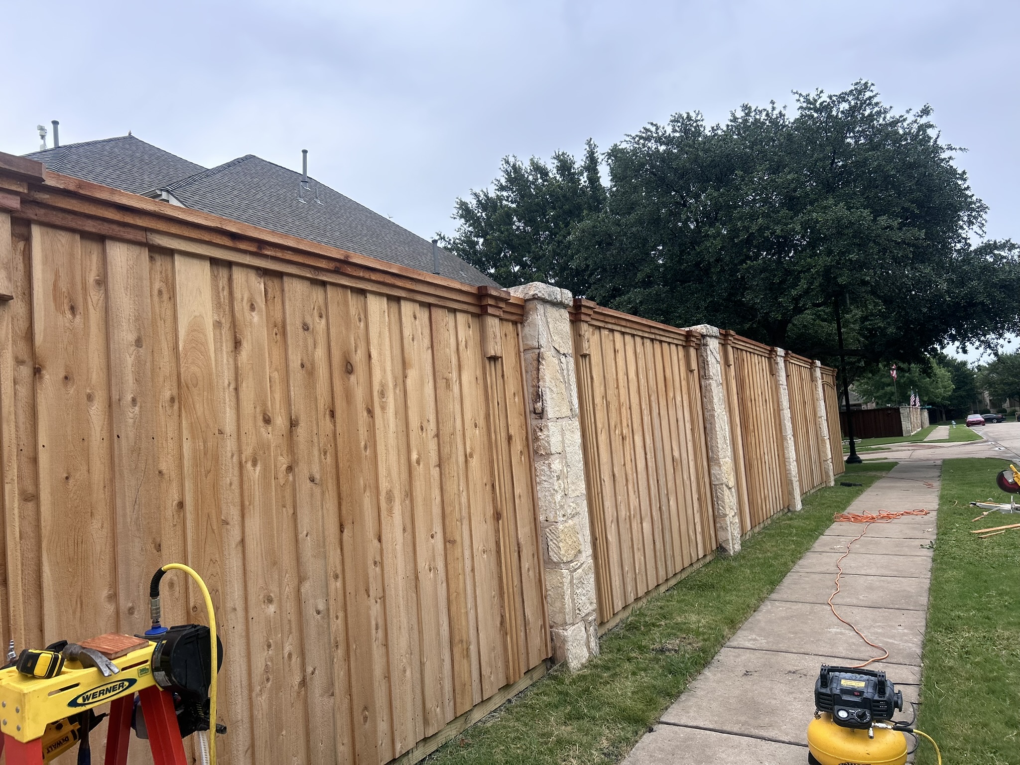New unstained cedar board-on-board fence with stone columns on sidewalk