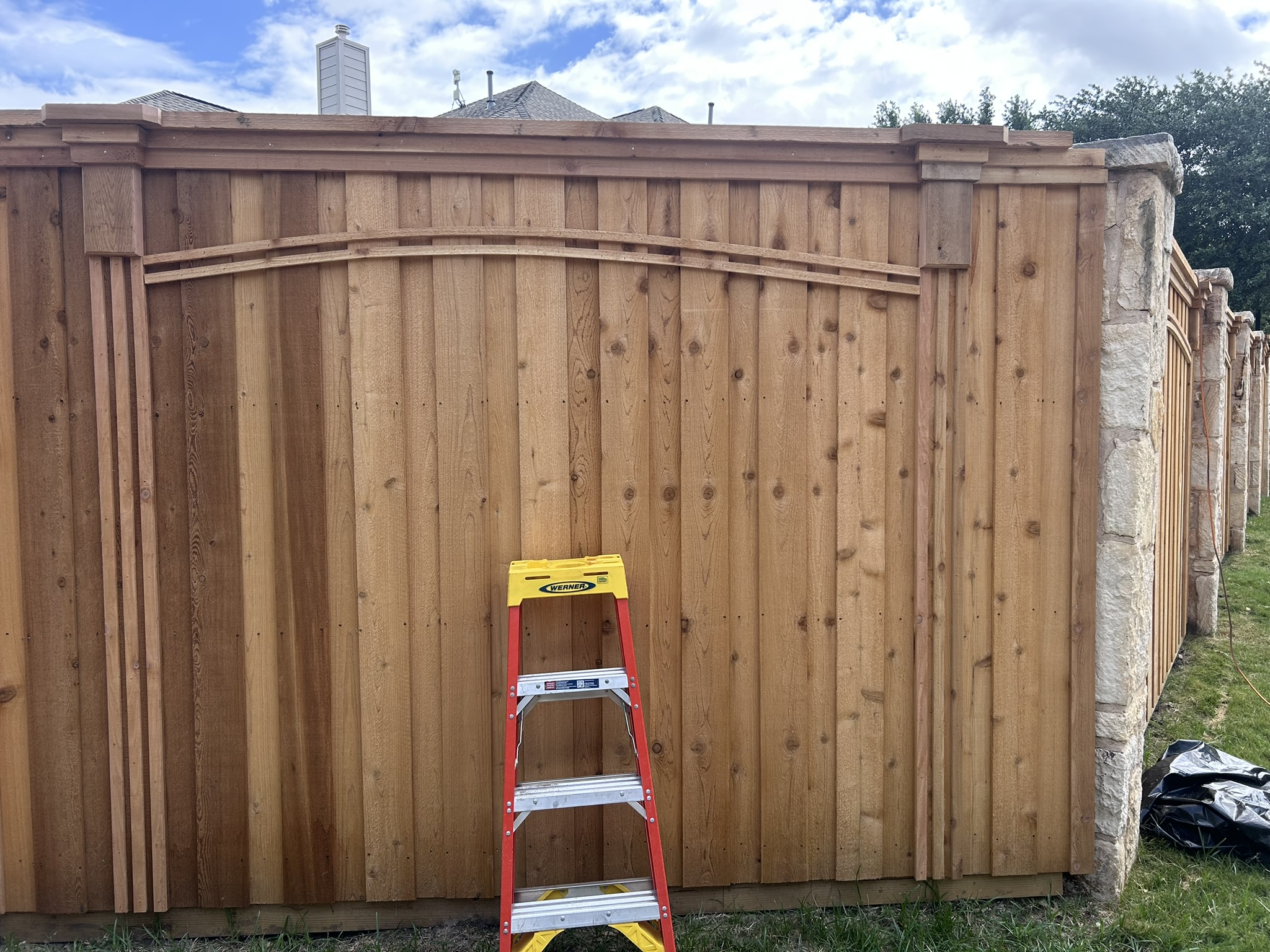 Close-up of new cedar fence panel with arched decorative top rail between stone columns