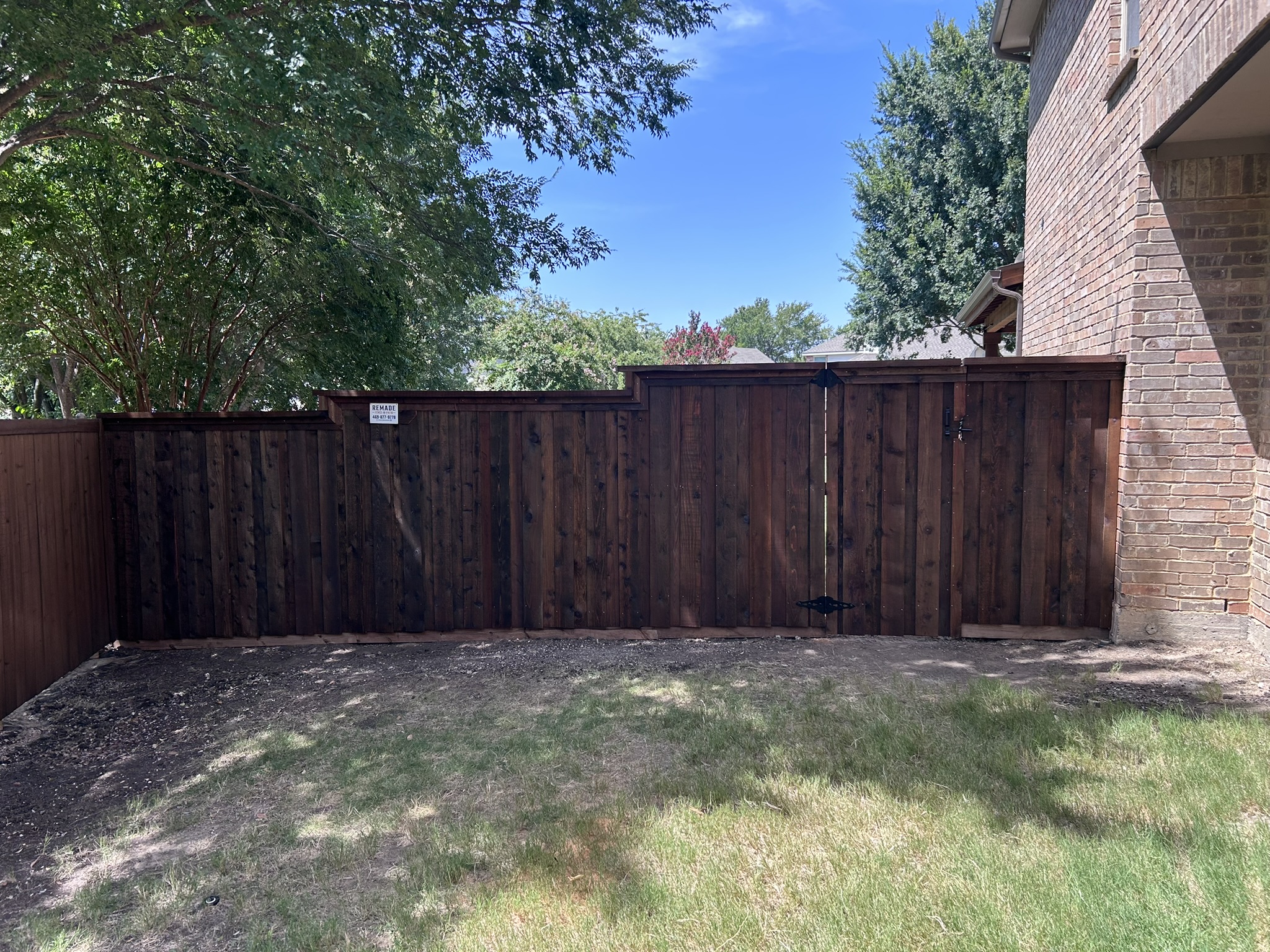 Dark-stained board-on-board wood privacy fence with gate along backyard of brick home