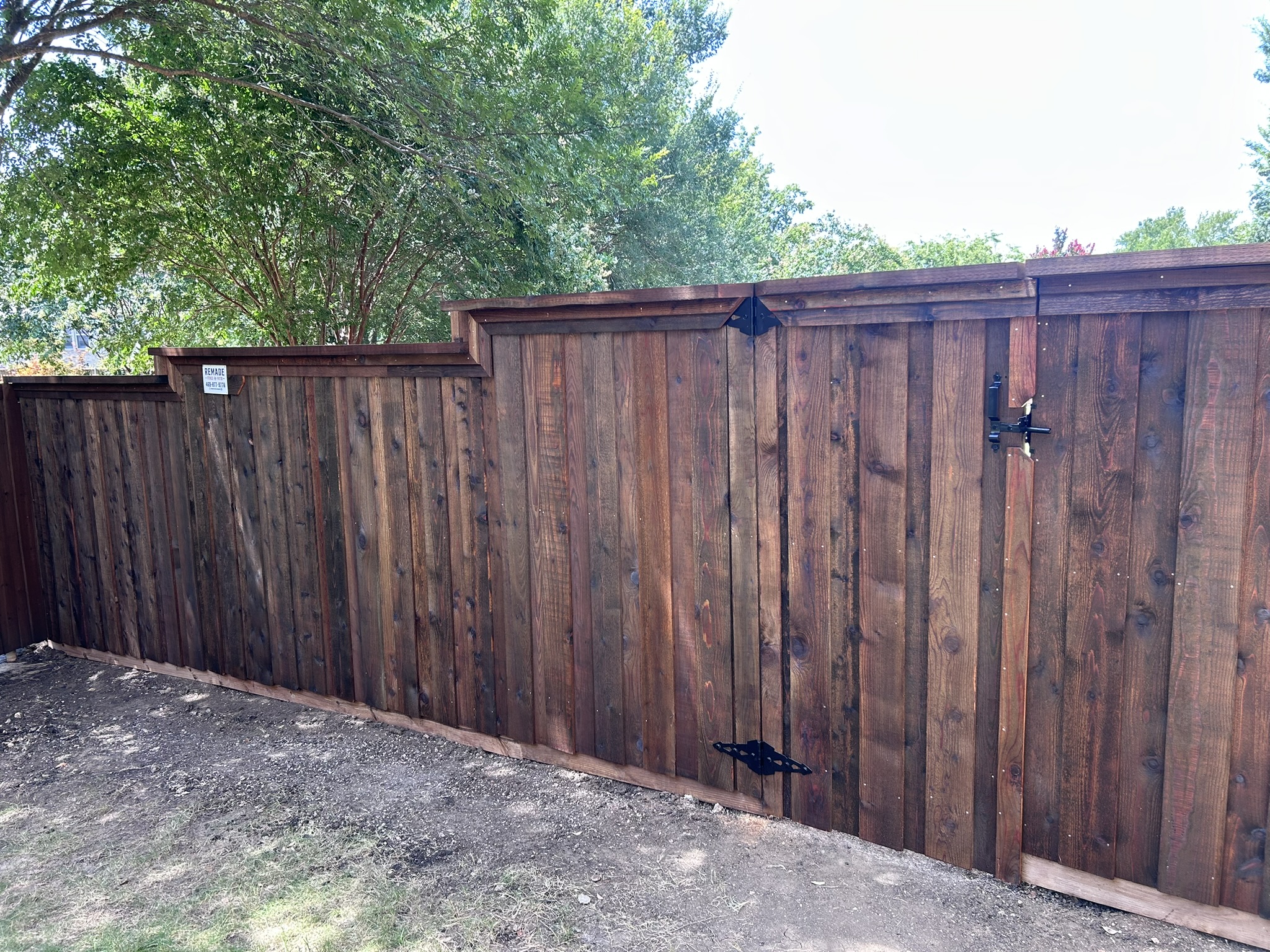 Dark-stained cedar board-on-board privacy fence with gate and decorative iron hinges