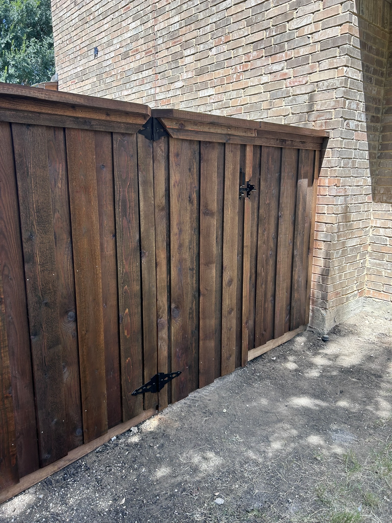 Dark-stained cedar wood gate with decorative iron hinges next to brick wall