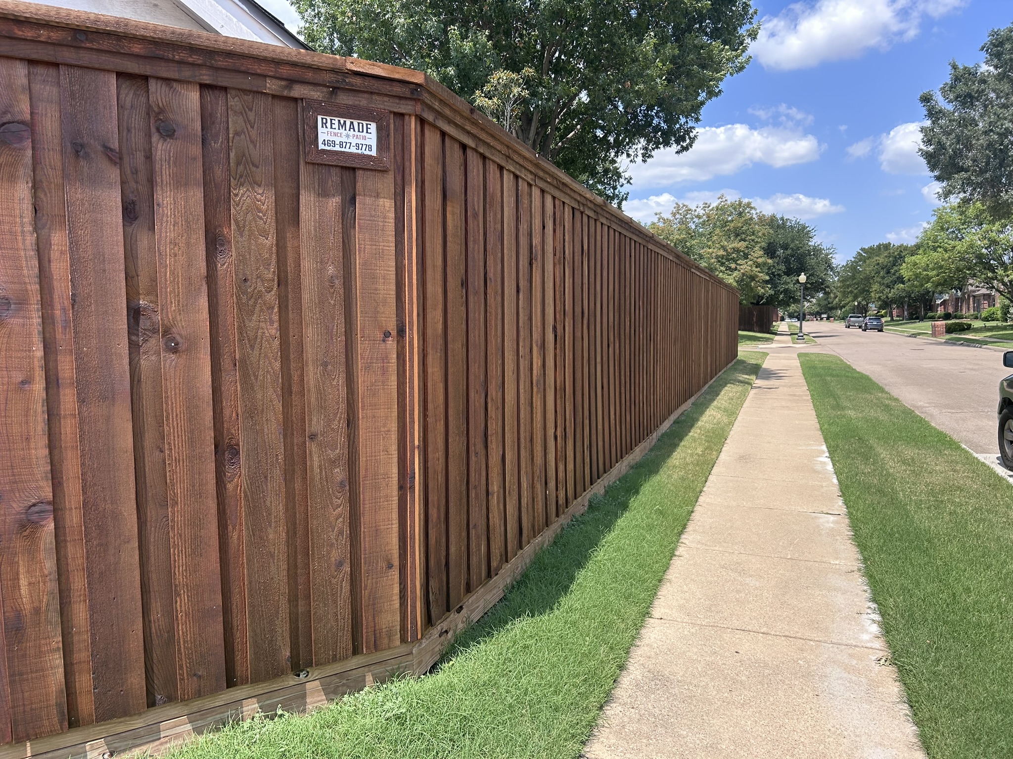 Stained cedar privacy fence with company sign along sidewalk