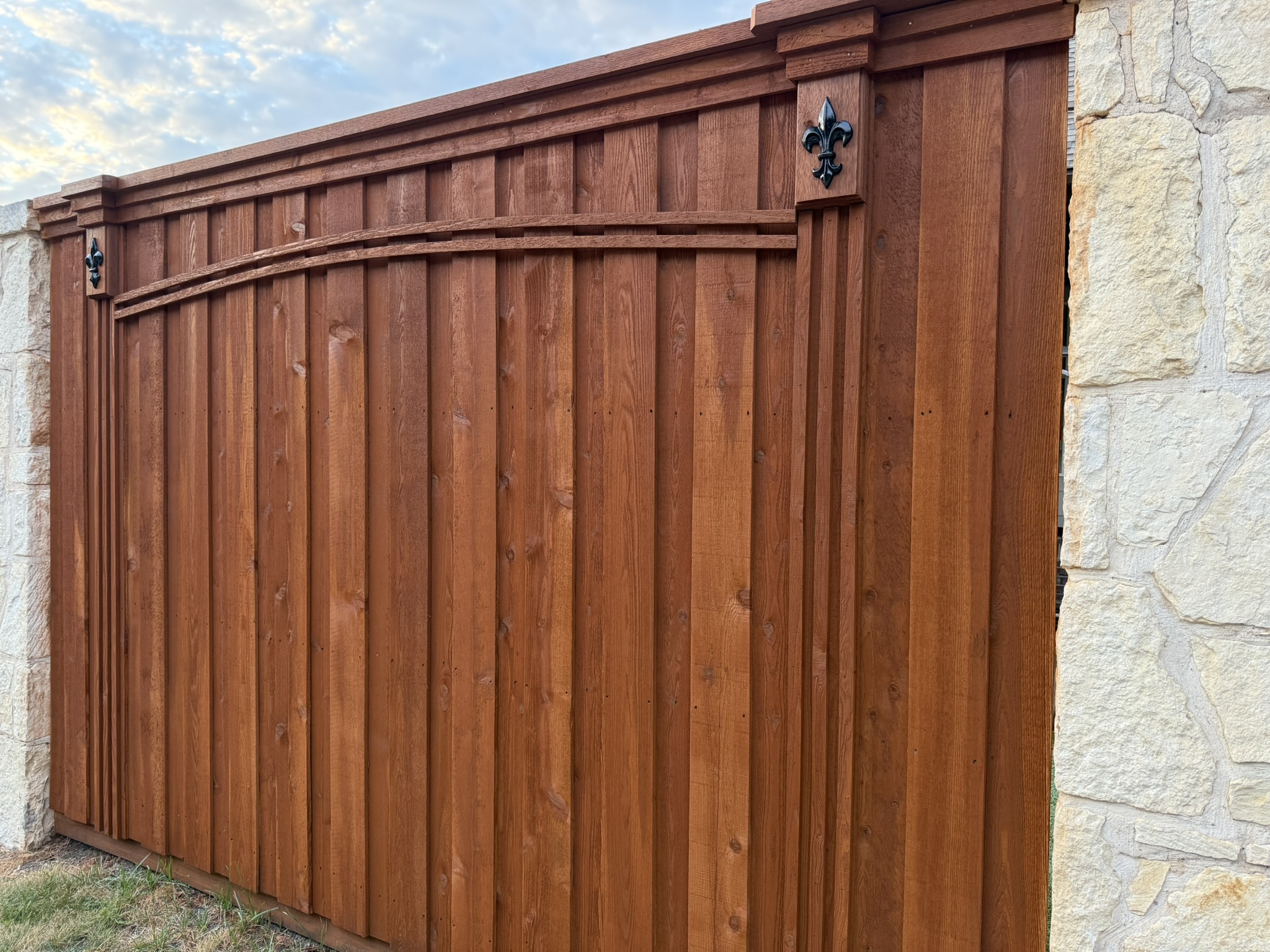 Stained cedar arched-top wood gate with decorative fleur-de-lis hardware