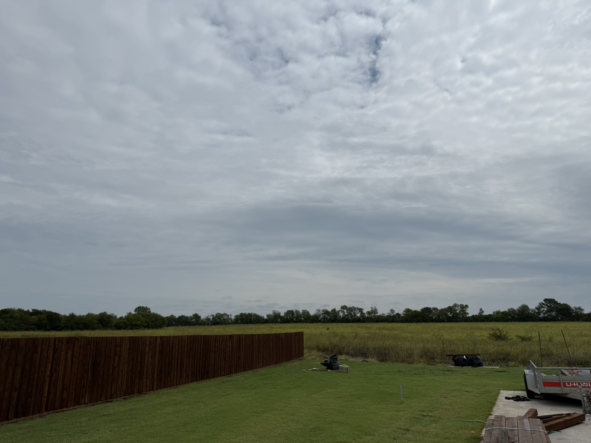 Stained cedar privacy fence in large rural property with open field
