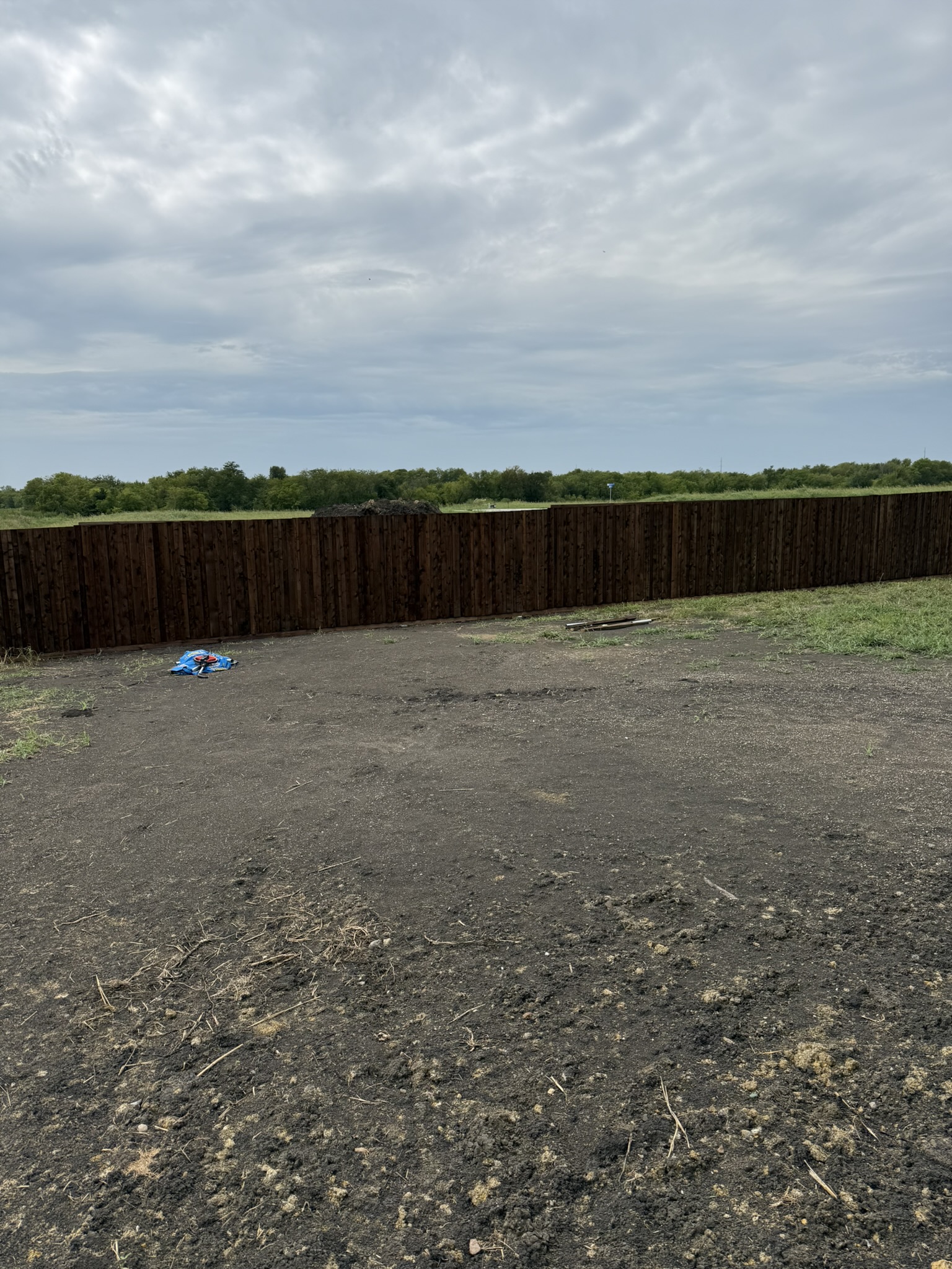 Stained cedar privacy fence viewed from distance across dirt lot