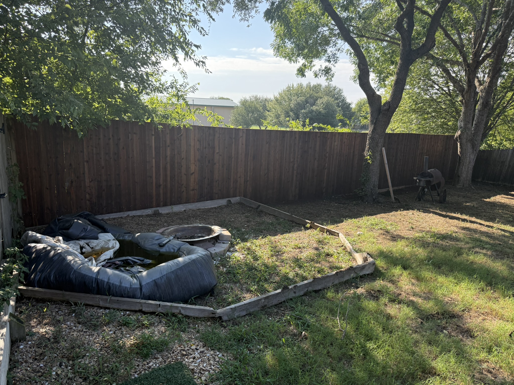 Stained cedar privacy fence in backyard with wheelbarrow and mature trees