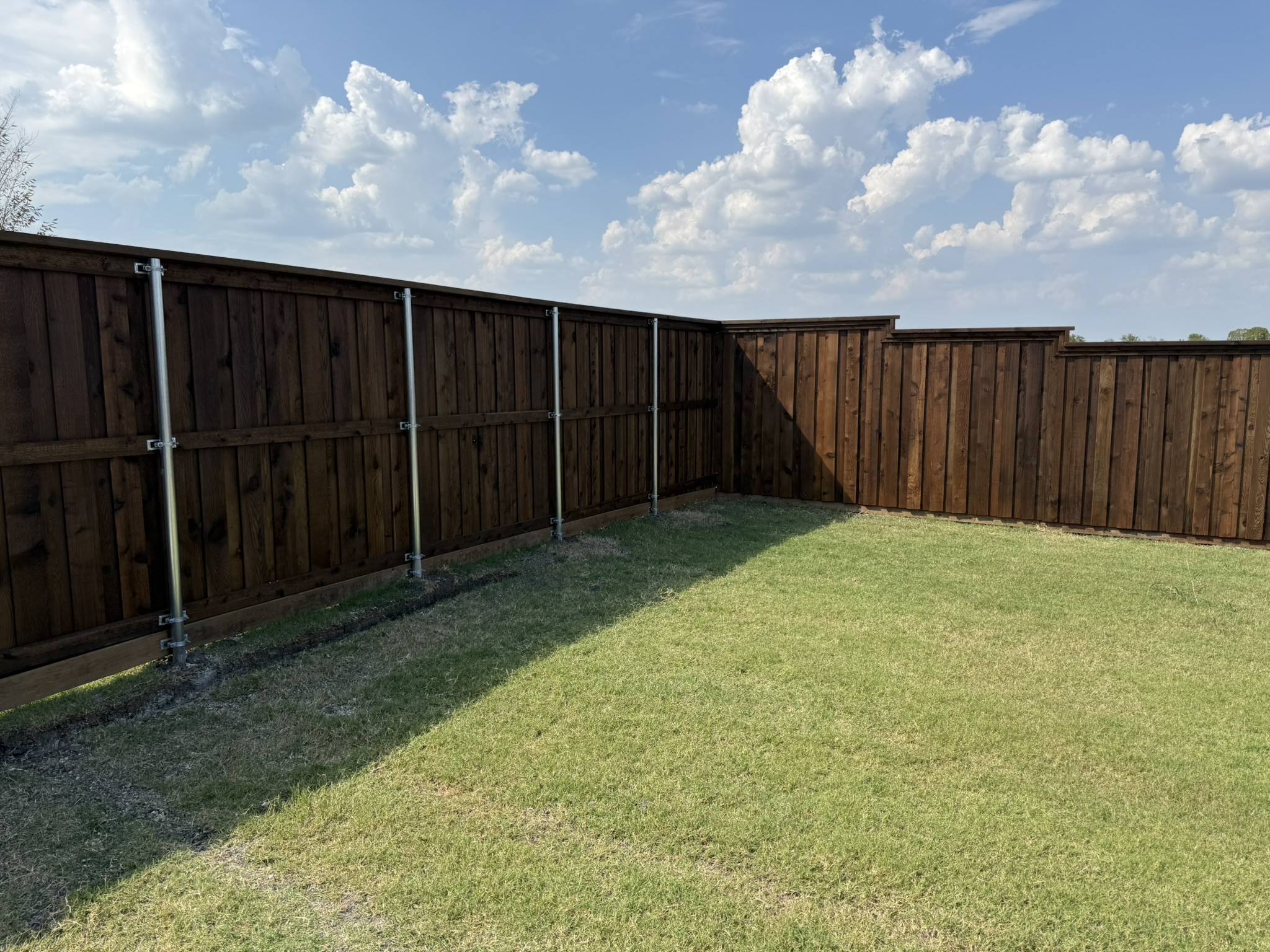 Long stained cedar privacy fence enclosing large backyard with green grass