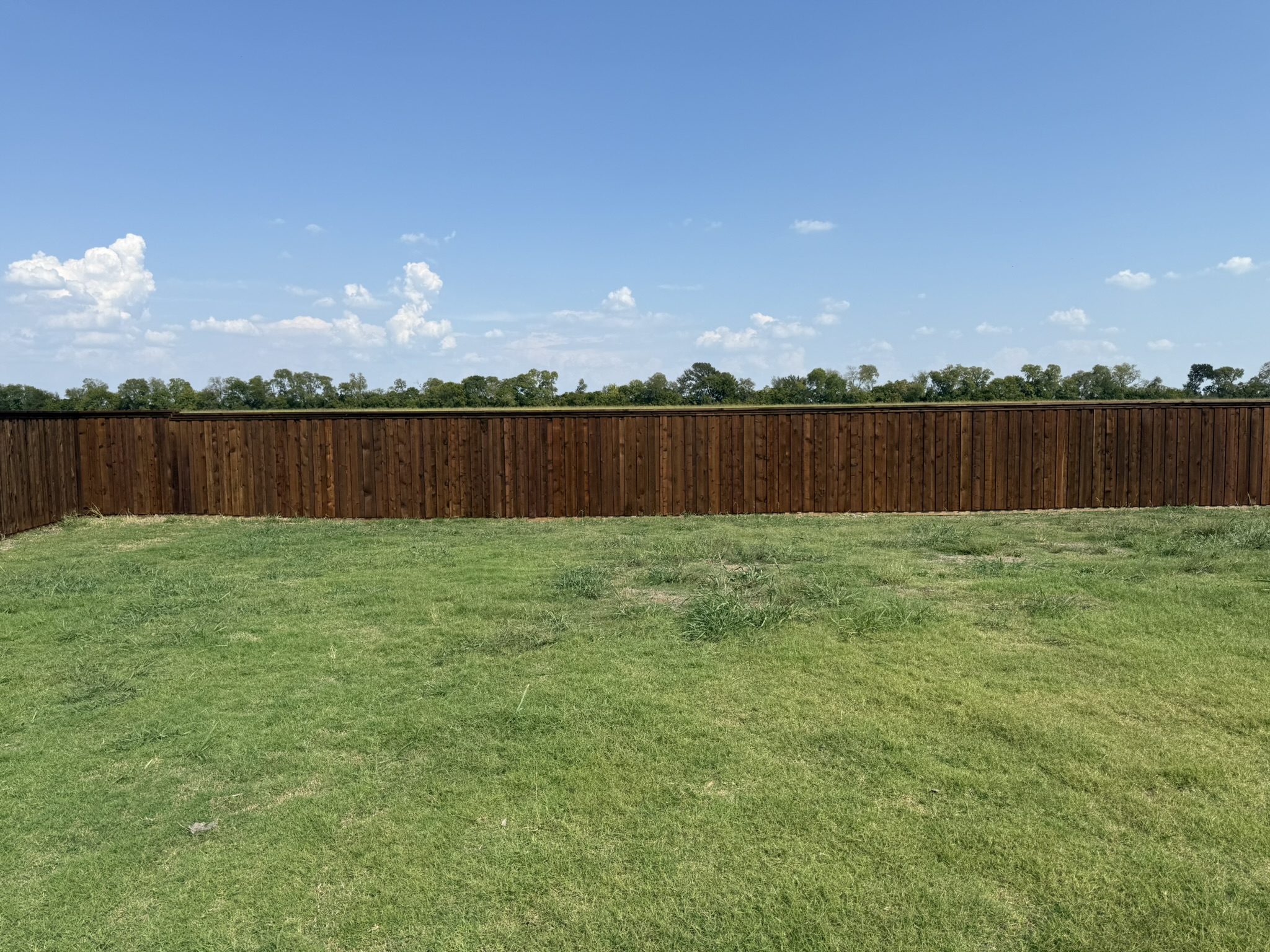 Stained cedar privacy fence at corner with height transition across rural lot