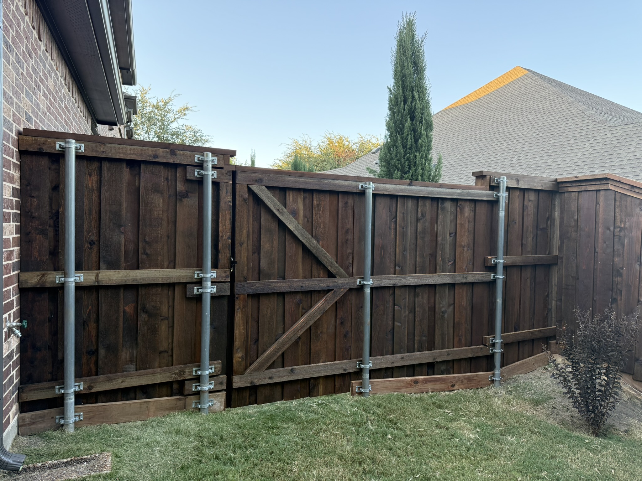 Dark-stained cedar privacy fence with yard sign in front of brick home