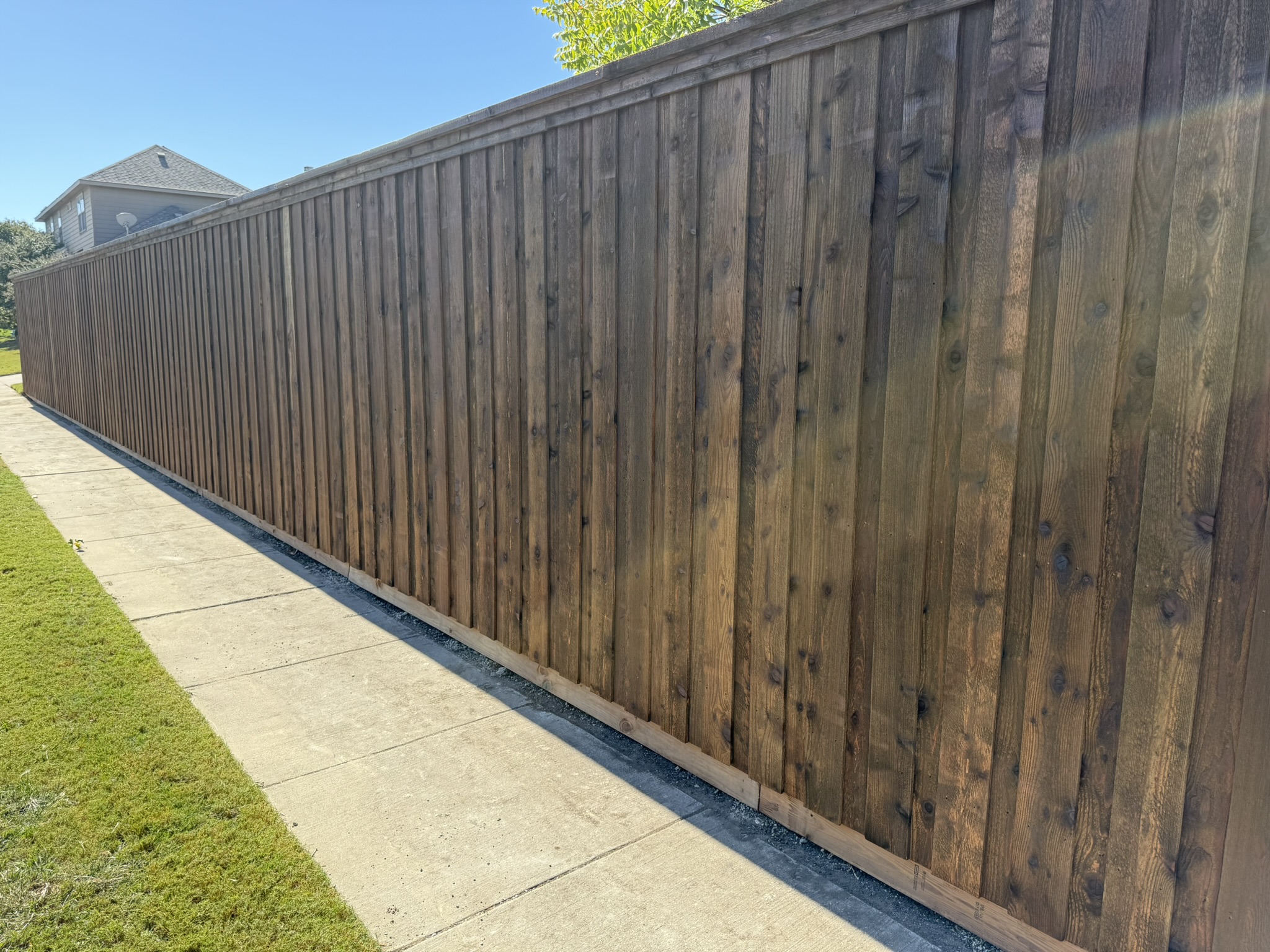 Back side of stained cedar fence showing metal posts on artificial turf