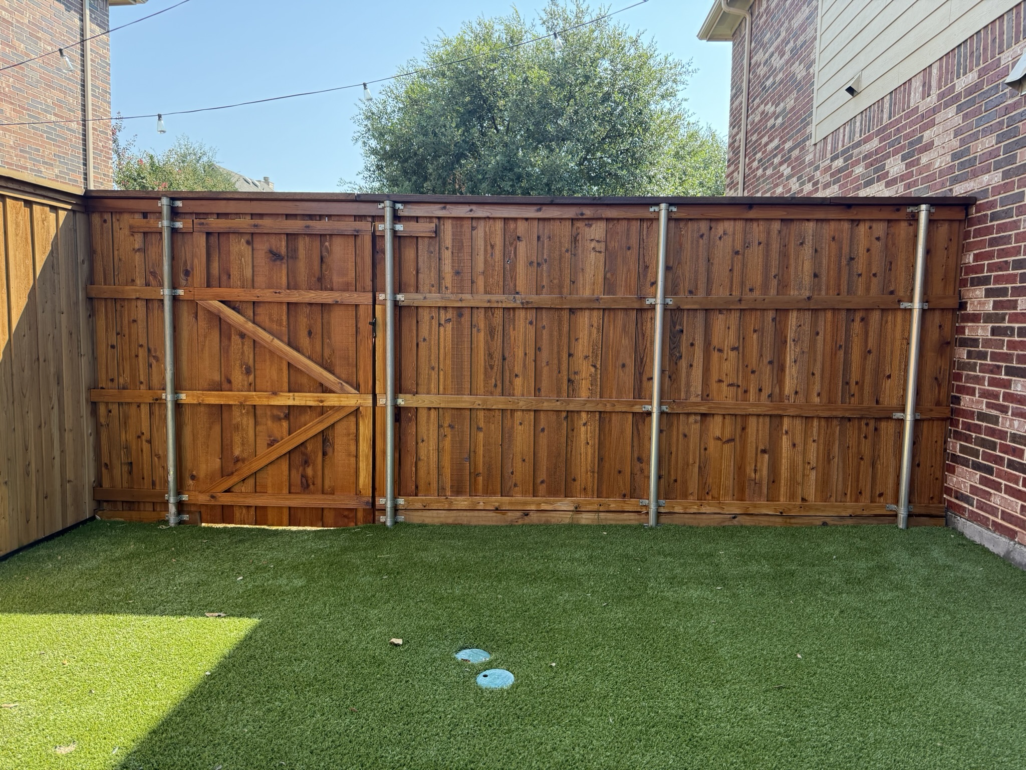 Back side of stained cedar privacy fence with metal posts curving along backyard