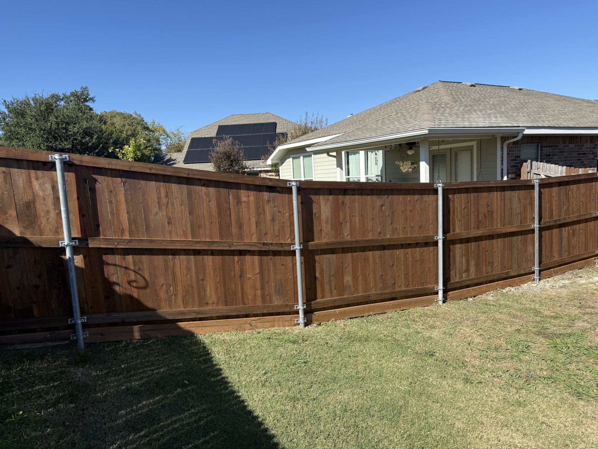 Dark-stained cedar privacy fence along flagstone walkway beside brick home
