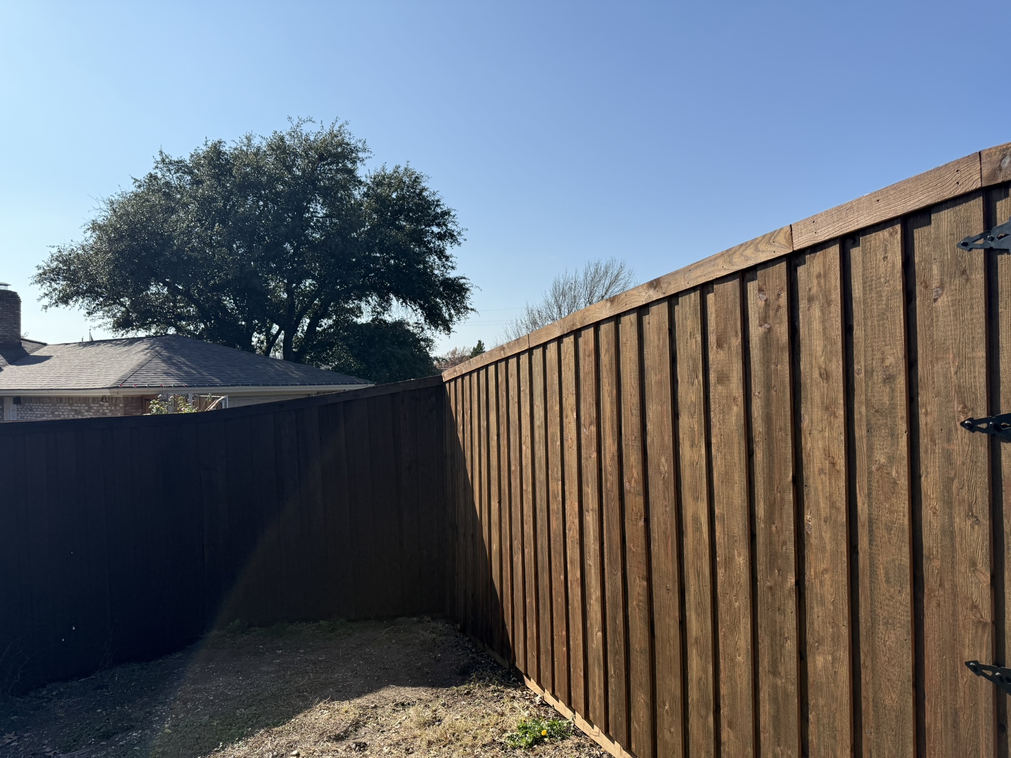 Dark-stained wood privacy fence and red-stained gate between brick homes