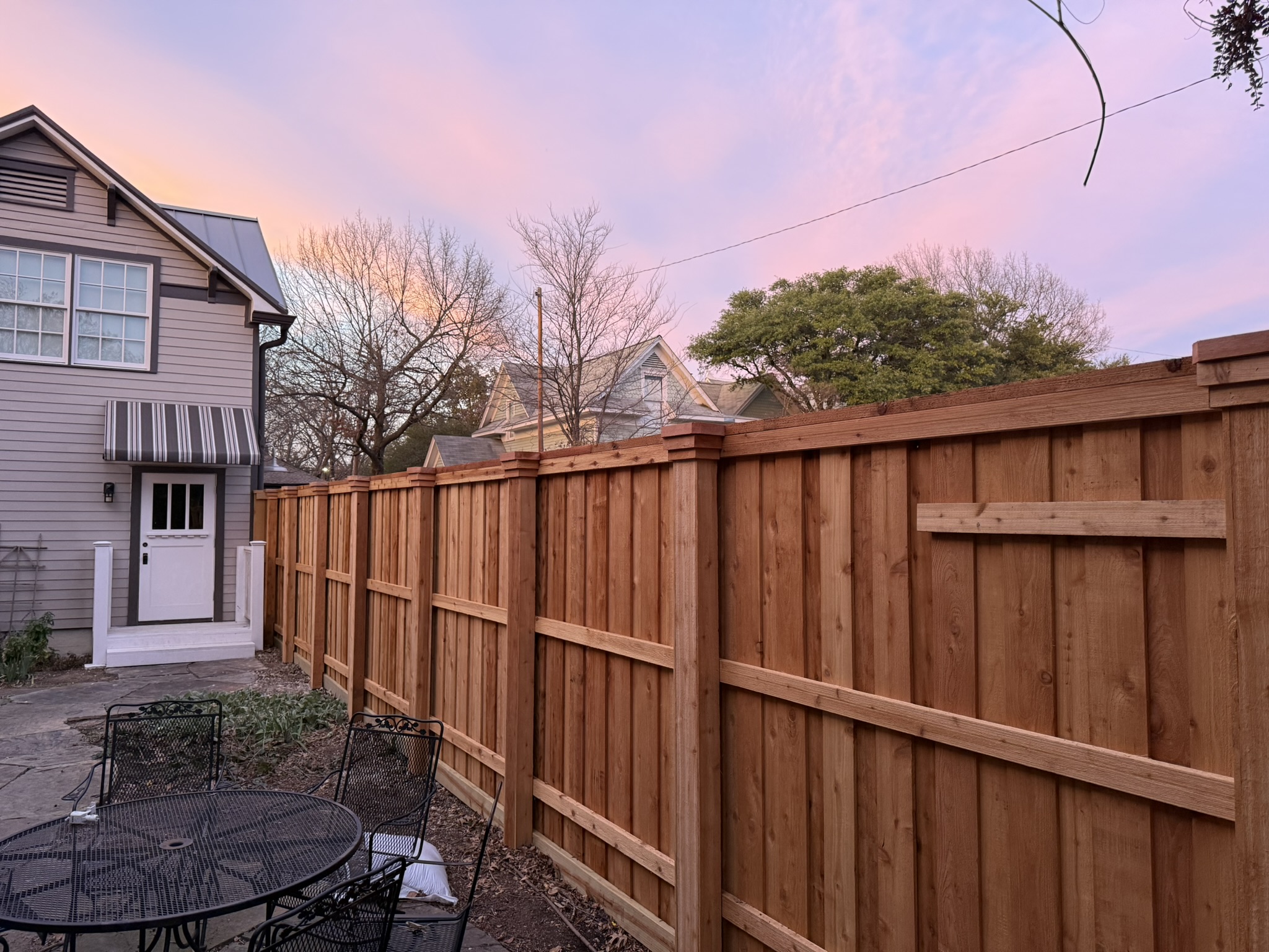 Dark-stained cedar privacy fence with company sign next to brick home