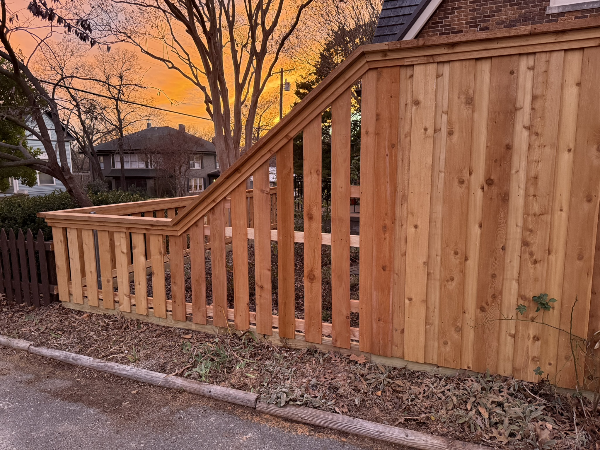 Stained cedar fence under construction with iron fence section in background
