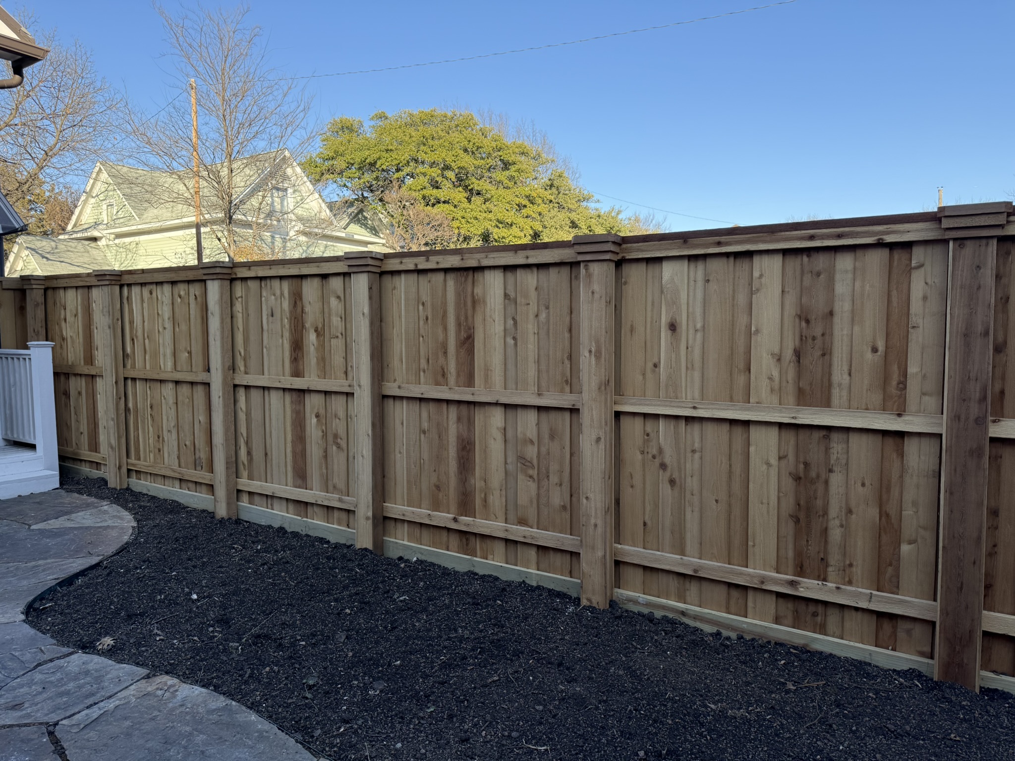 Stained cedar board-on-board privacy fence in backyard with mature trees